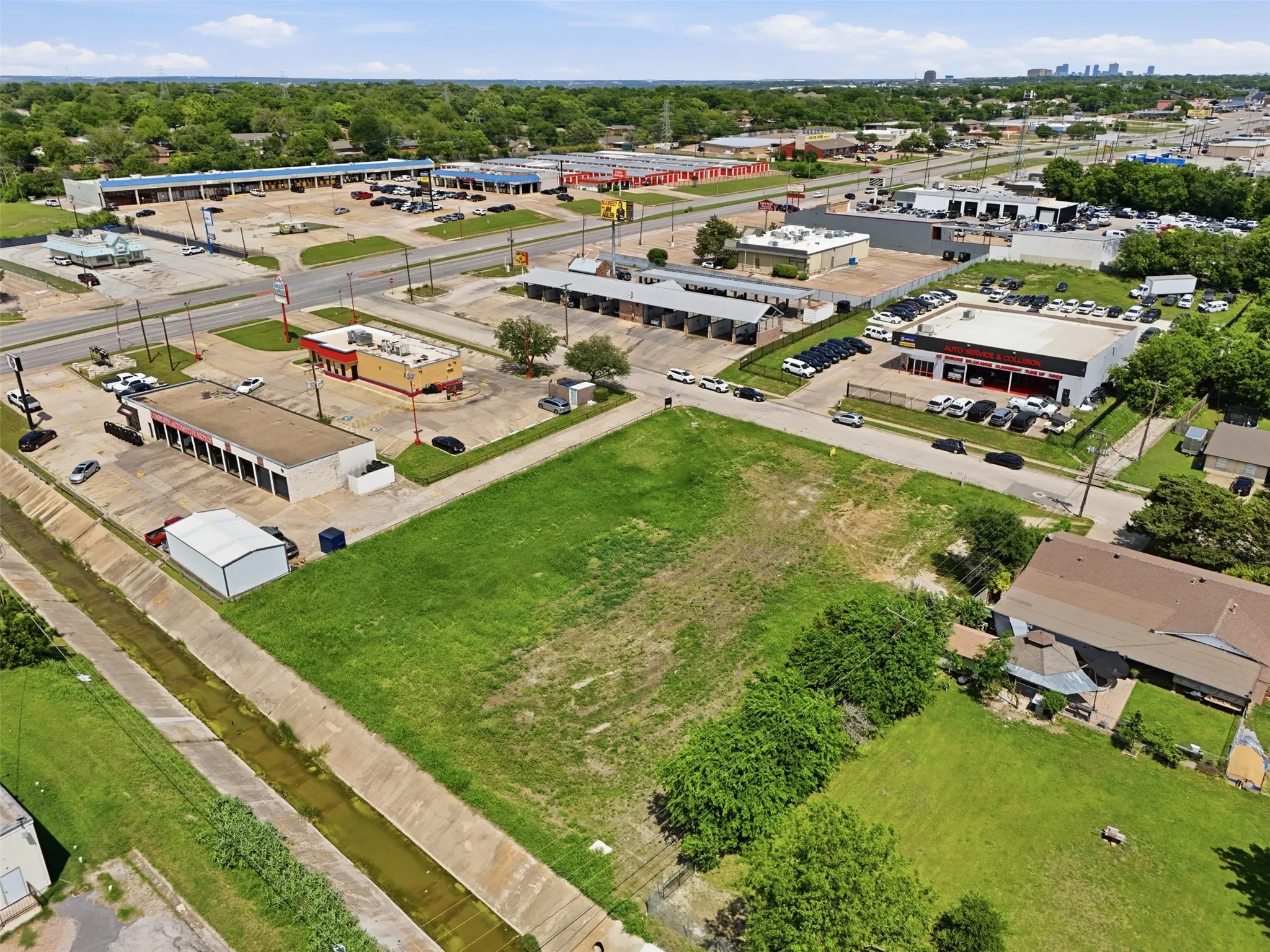Expansive green space featuring clear land, adjacent commercial properties, established roads, and a visible concrete channel