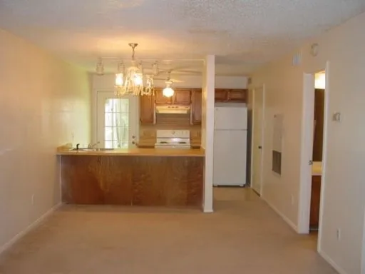 Carpeted living space opening to a kitchen featuring wood cabinetry, white appliances, and a wood-finish breakfast bar