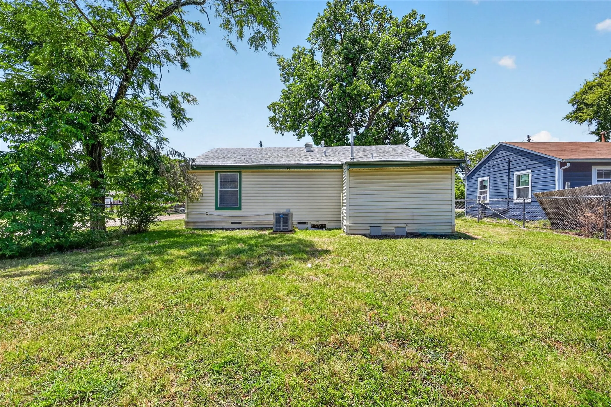 Rear exterior featuring cream siding, green trim, a single window, and a visible HVAC unit