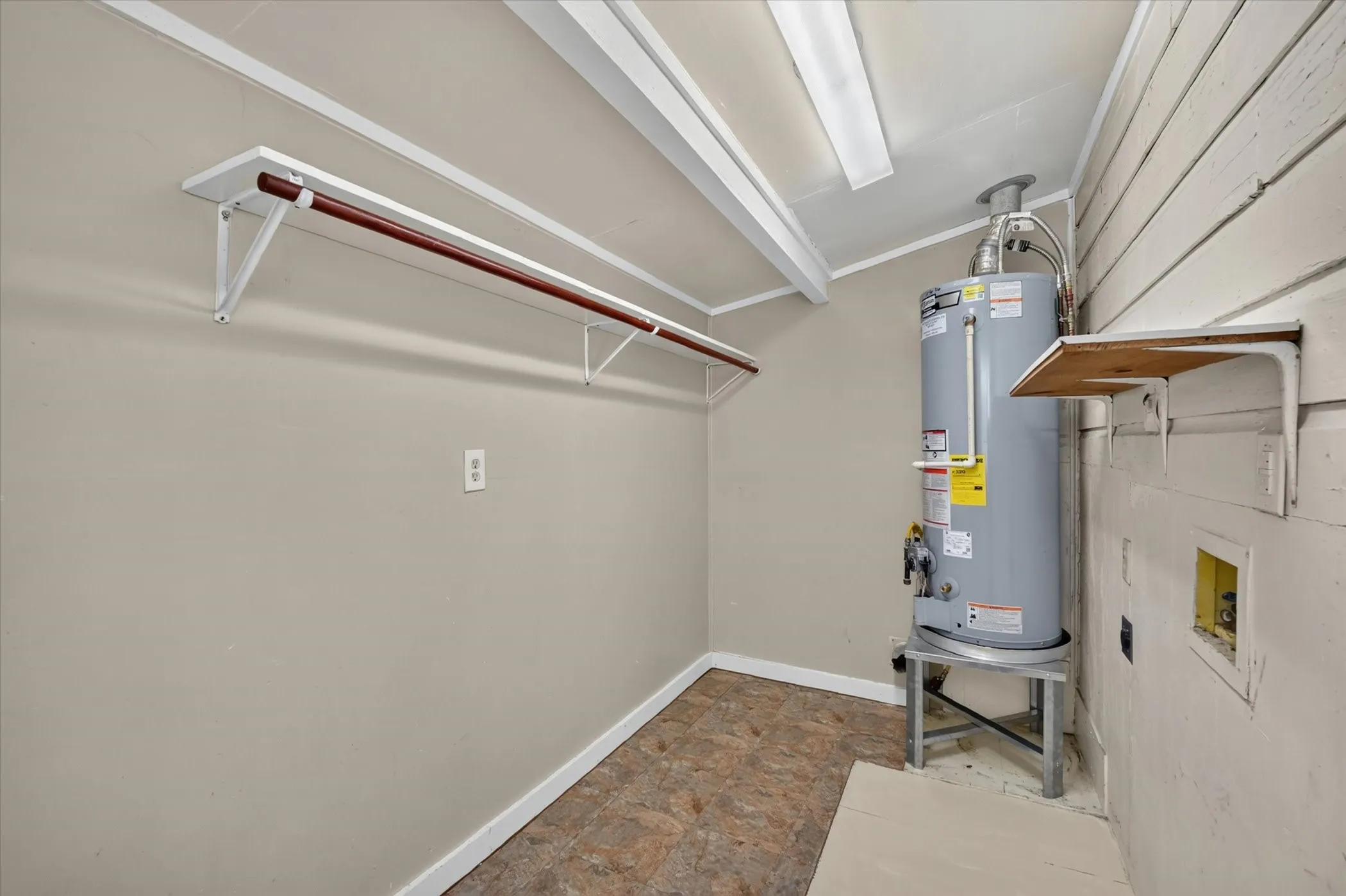 Laundry area featuring water heater, wall-mounted shelving, and clothes hanging rod