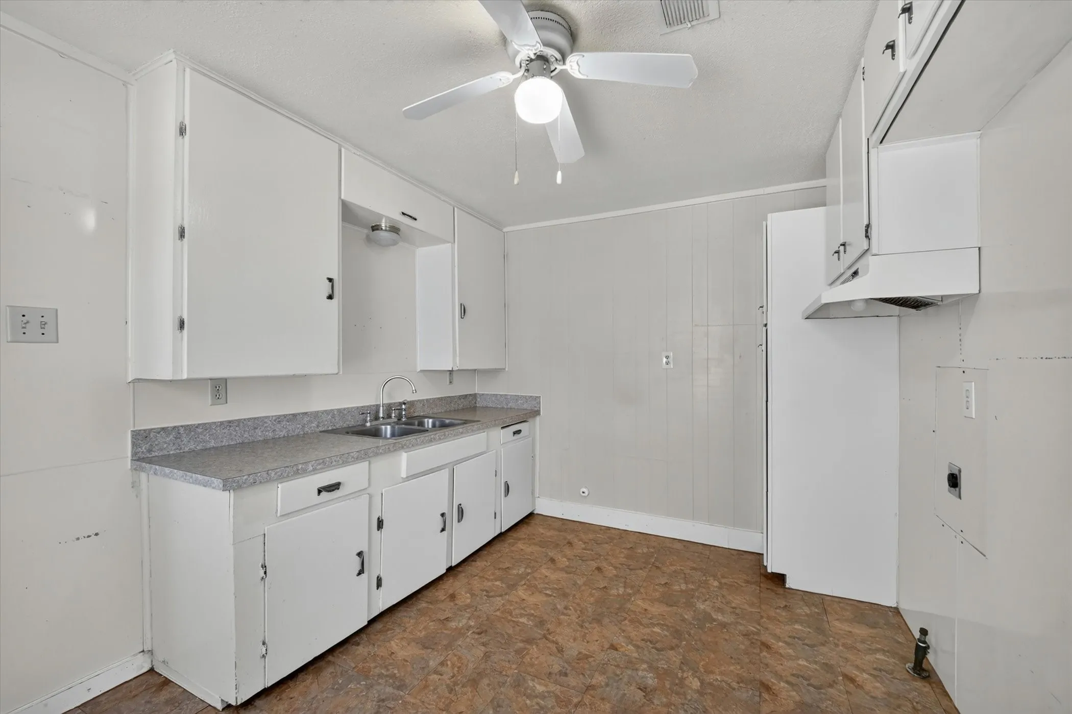 Kitchen featuring white cabinetry, a dual basin stainless steel sink, a gray speckled countertop, and resilient flooring