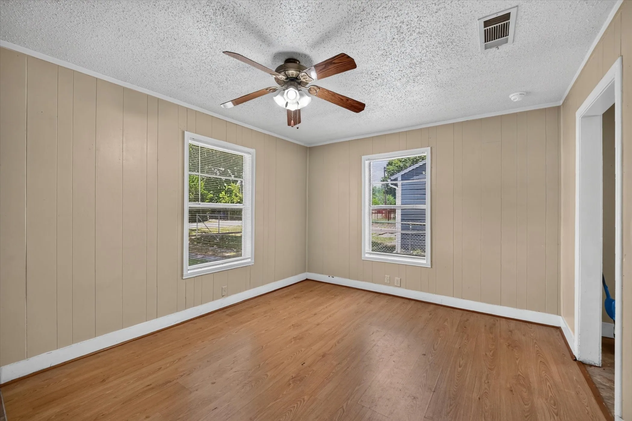 Room featuring wood-finish flooring, two large windows, a ceiling fan with integrated lighting, and board-and-batten wall paneling
