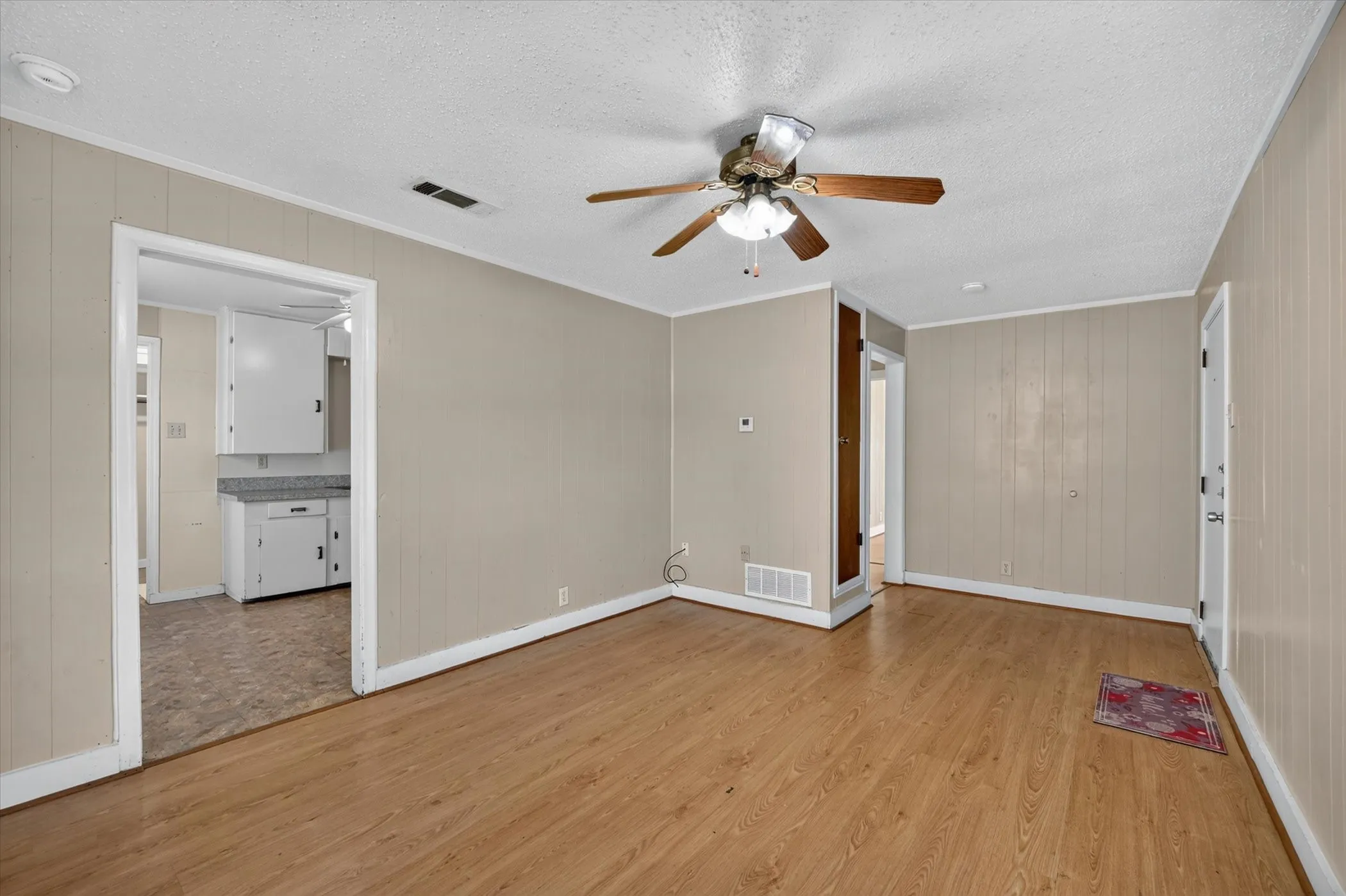 Open concept living area featuring wood-finish flooring, neutral wall paneling, and a ceiling fan