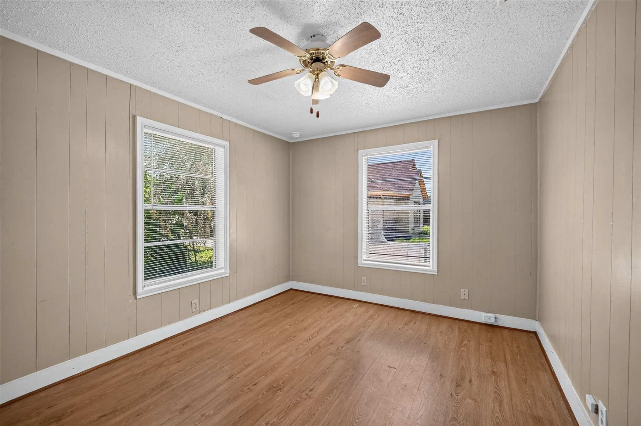 Room featuring wood-finish flooring, two windows with blinds, a ceiling fan with integrated lighting, and paneling walls