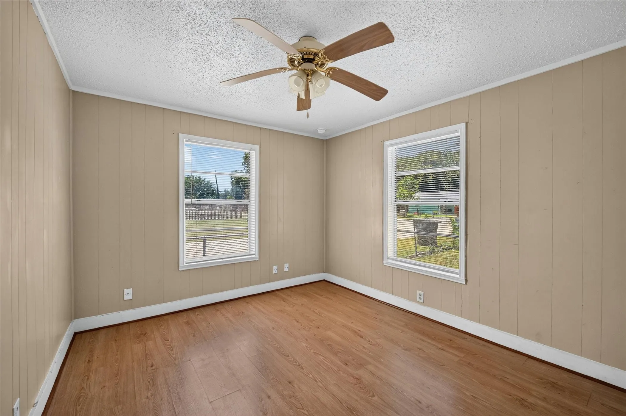 Room featuring wood-finish flooring, two large windows, a ceiling fan with light fixture, and vertical paneling walls