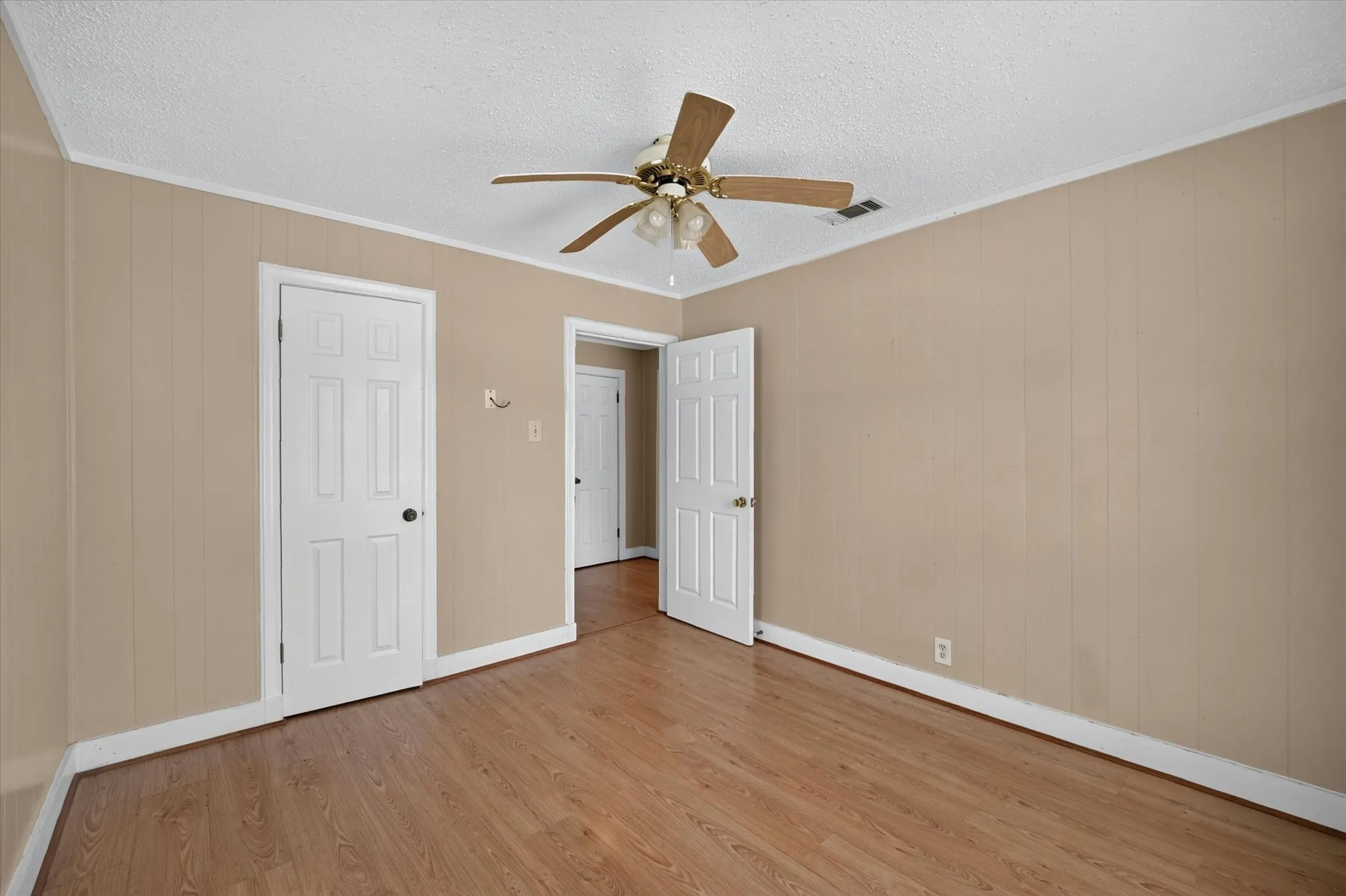 Interior room featuring wood-finish flooring, light beige paneled walls, and white trim