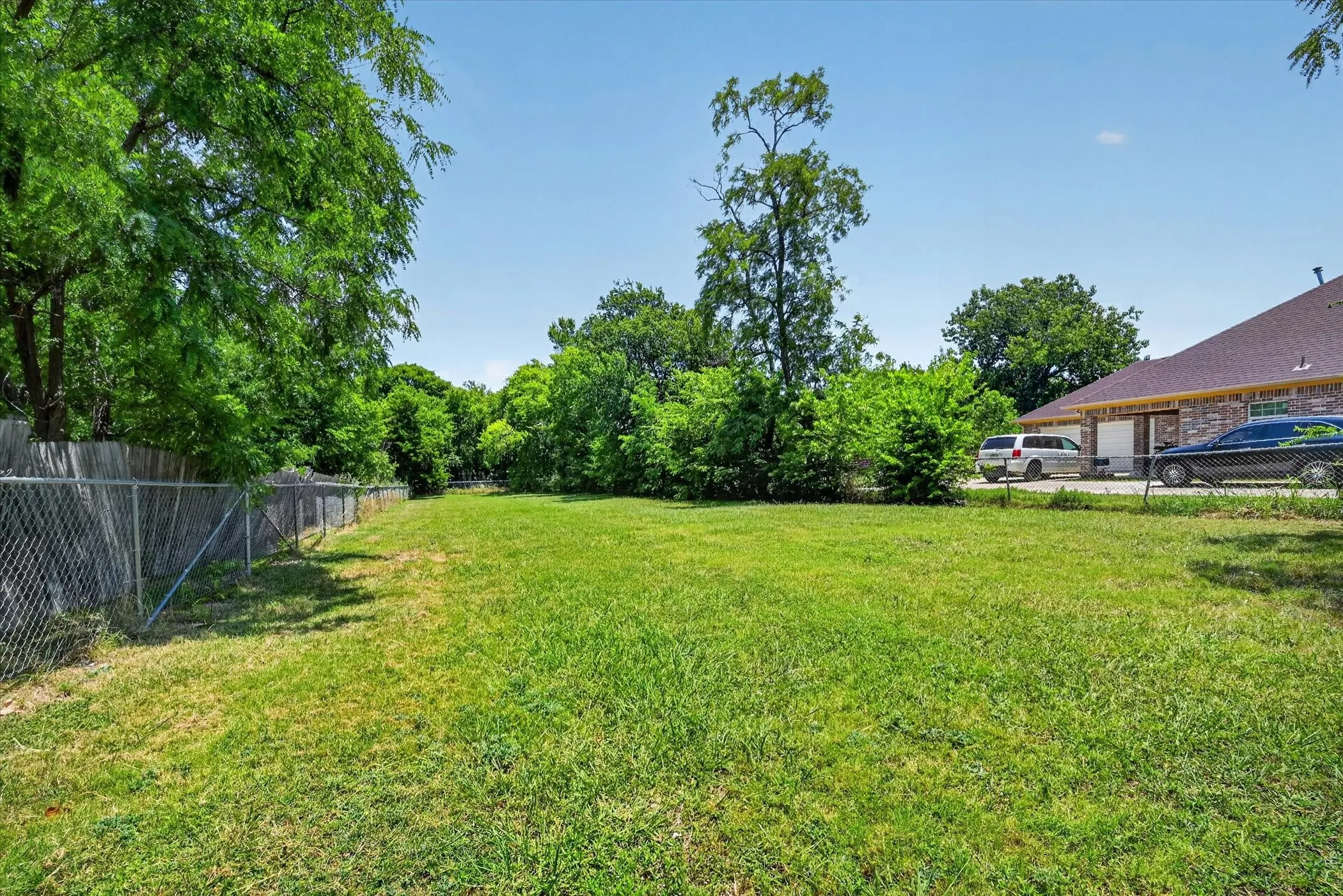 Expansive green lawn with mature trees and a chain-link fence bordering the property