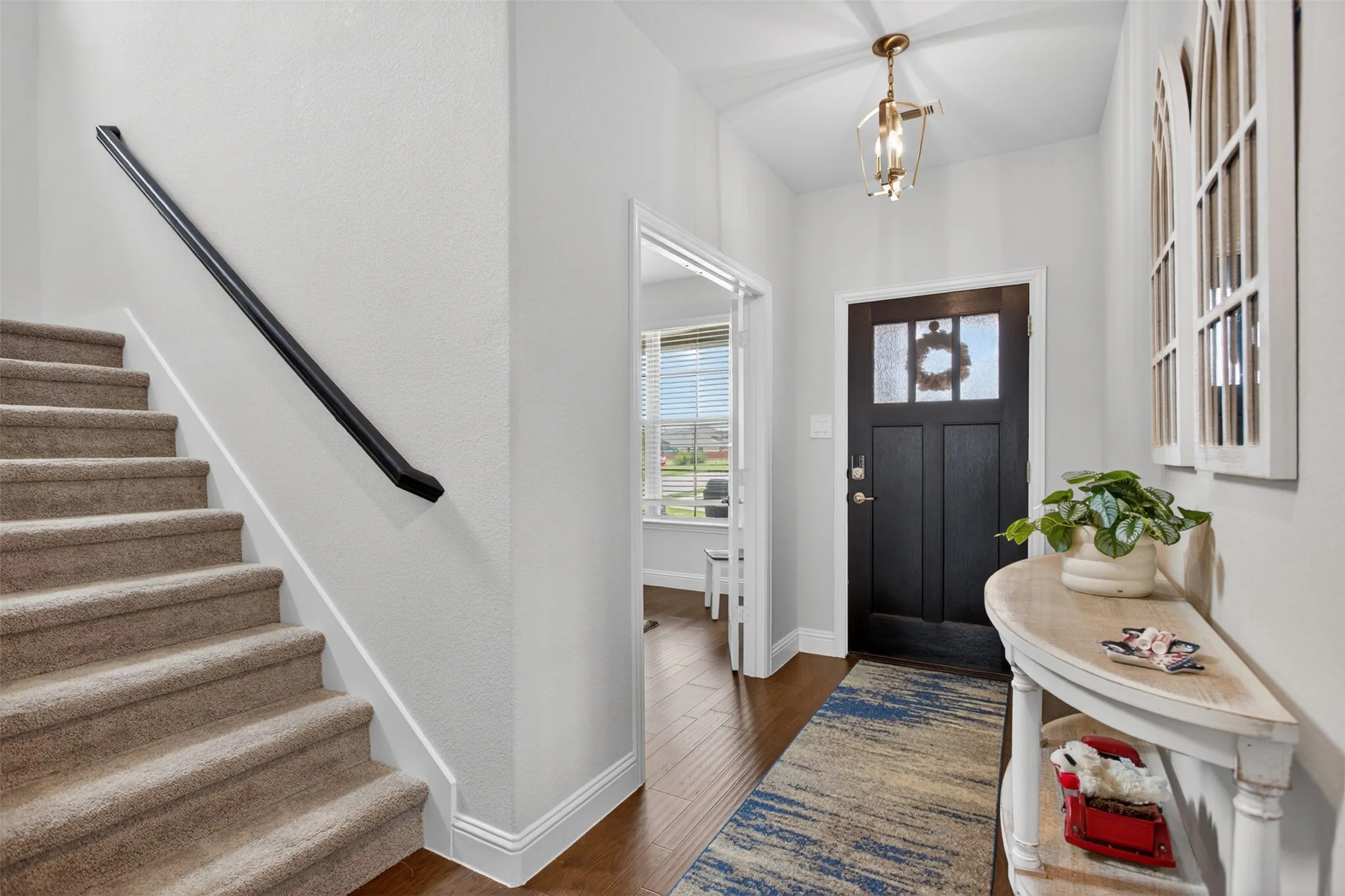 Foyer featuring a dark wood-finish entry door with glass inserts, wood-finish flooring, a contemporary ceiling light fixture, and a carpeted staircase with a black handrail