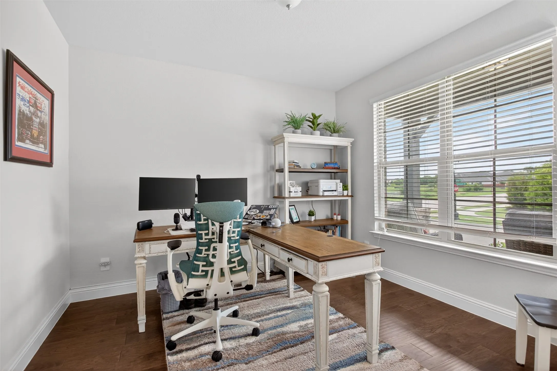Bright interior room featuring a large window with horizontal blinds, wood-finish flooring, and white walls