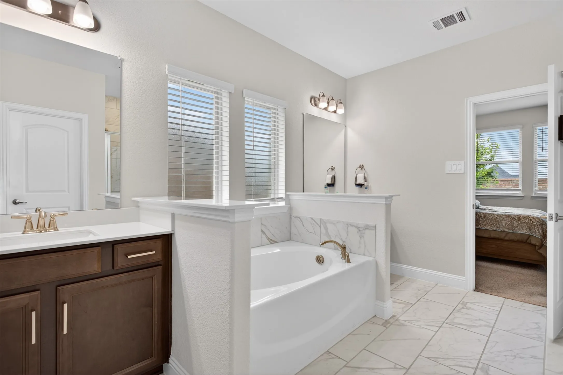 Bathroom featuring a soaking tub with a tiled surround, a single vanity with a quartz countertop, wood-finish cabinetry, and tiled flooring