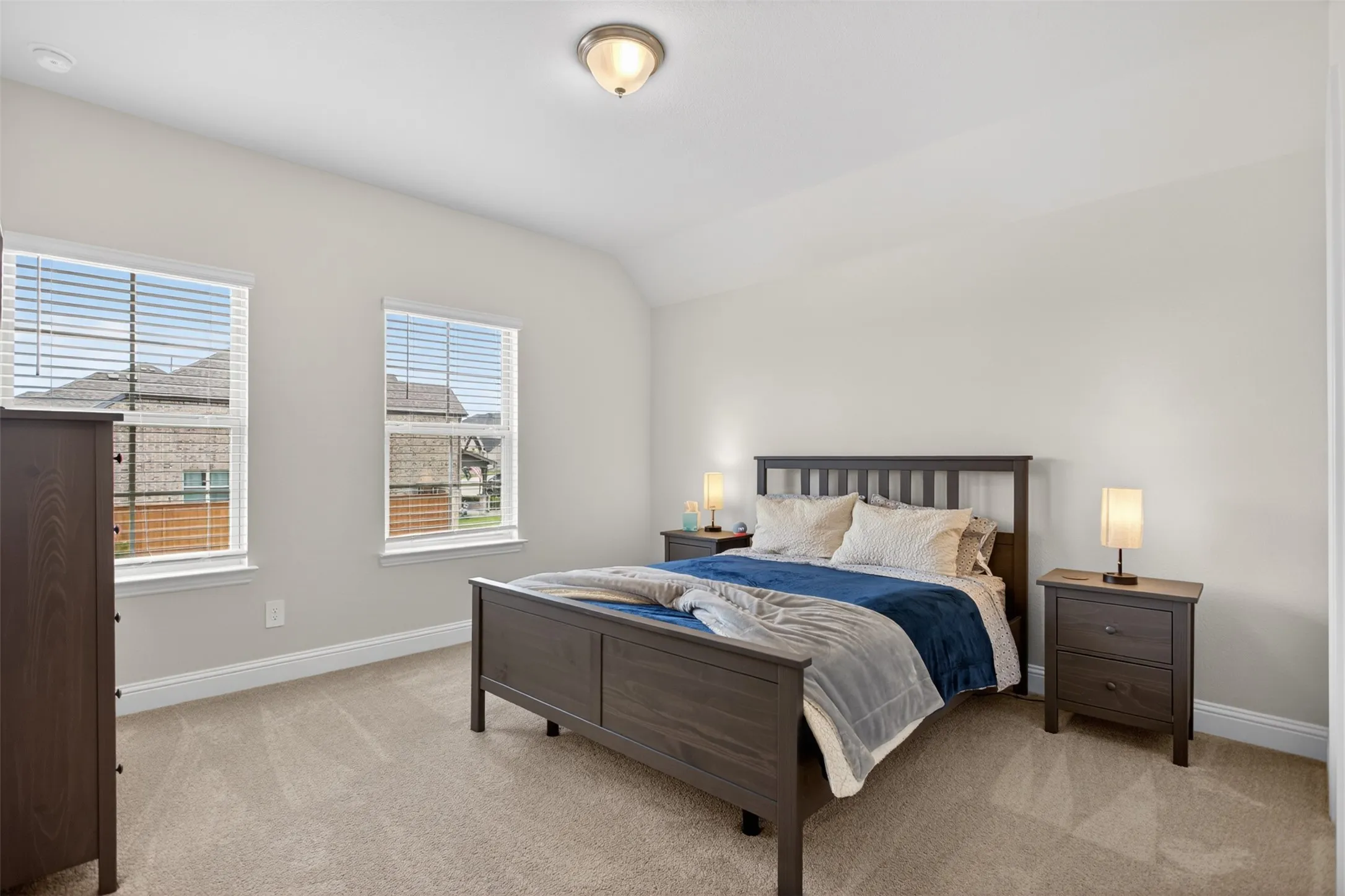 Carpeted bedroom featuring two large windows with blinds, a neutral wall color, and a ceiling-mounted light fixture