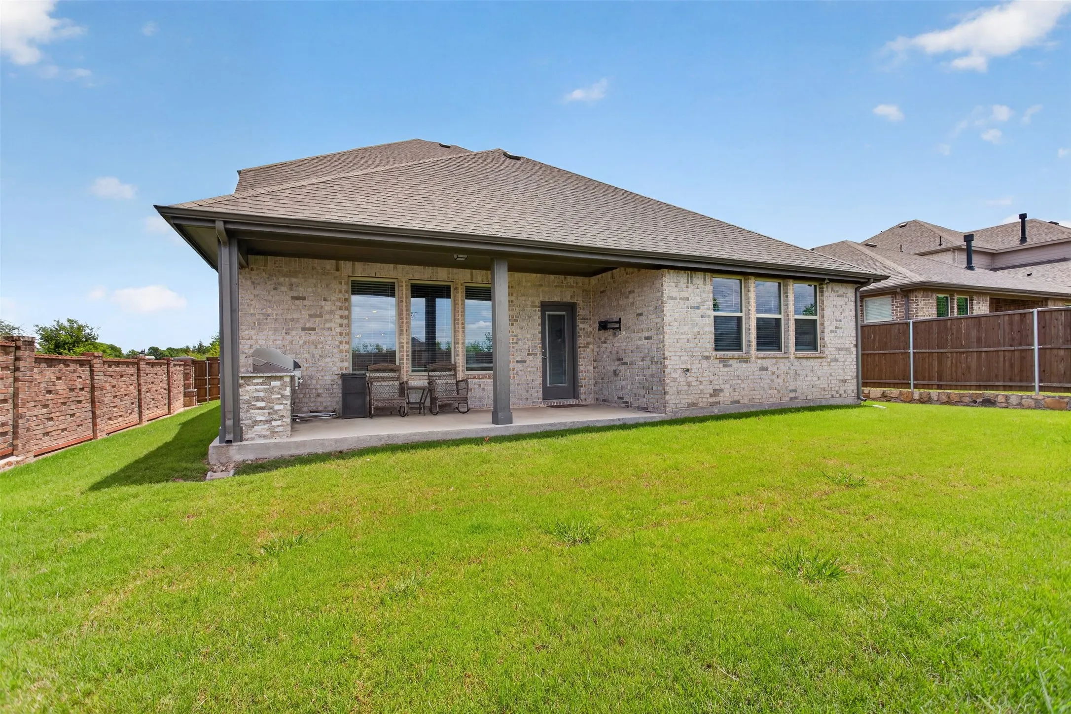 Expansive backyard featuring a covered patio with brick columns, a built-in stone grill station, and a concrete patio surface