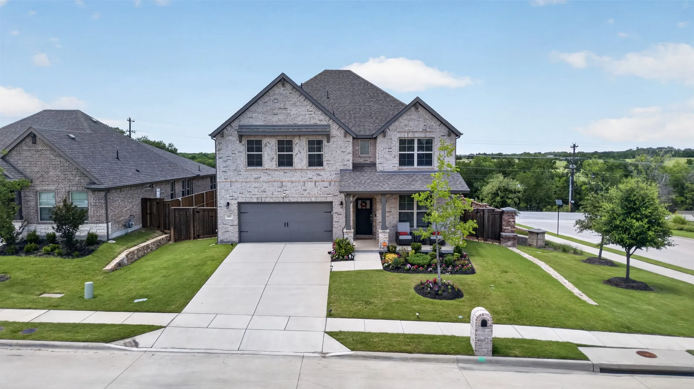 Two-story residence featuring a light-colored brick facade, a dark gray shingled roof, an attached two-car garage, and a concrete driveway