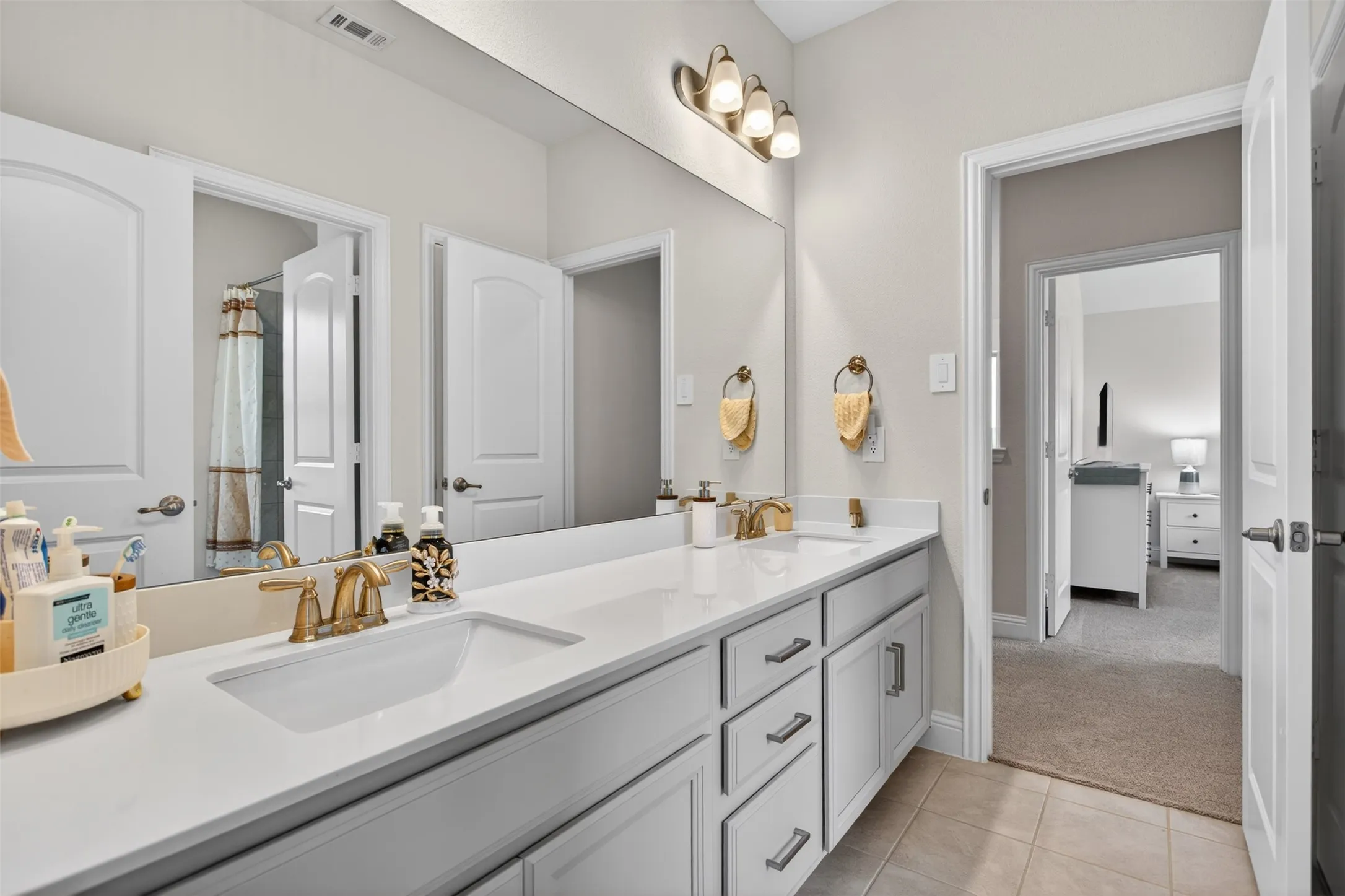 Dual vanity featuring white shaker cabinetry, gold-finish fixtures, and a continuous surface countertop