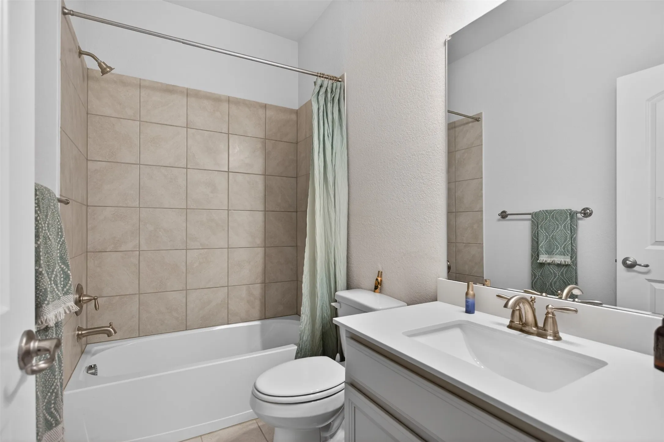 Bathroom featuring a white vanity with an integrated sink, brushed nickel fixtures, a ceramic tile shower surround, and a white bathtub