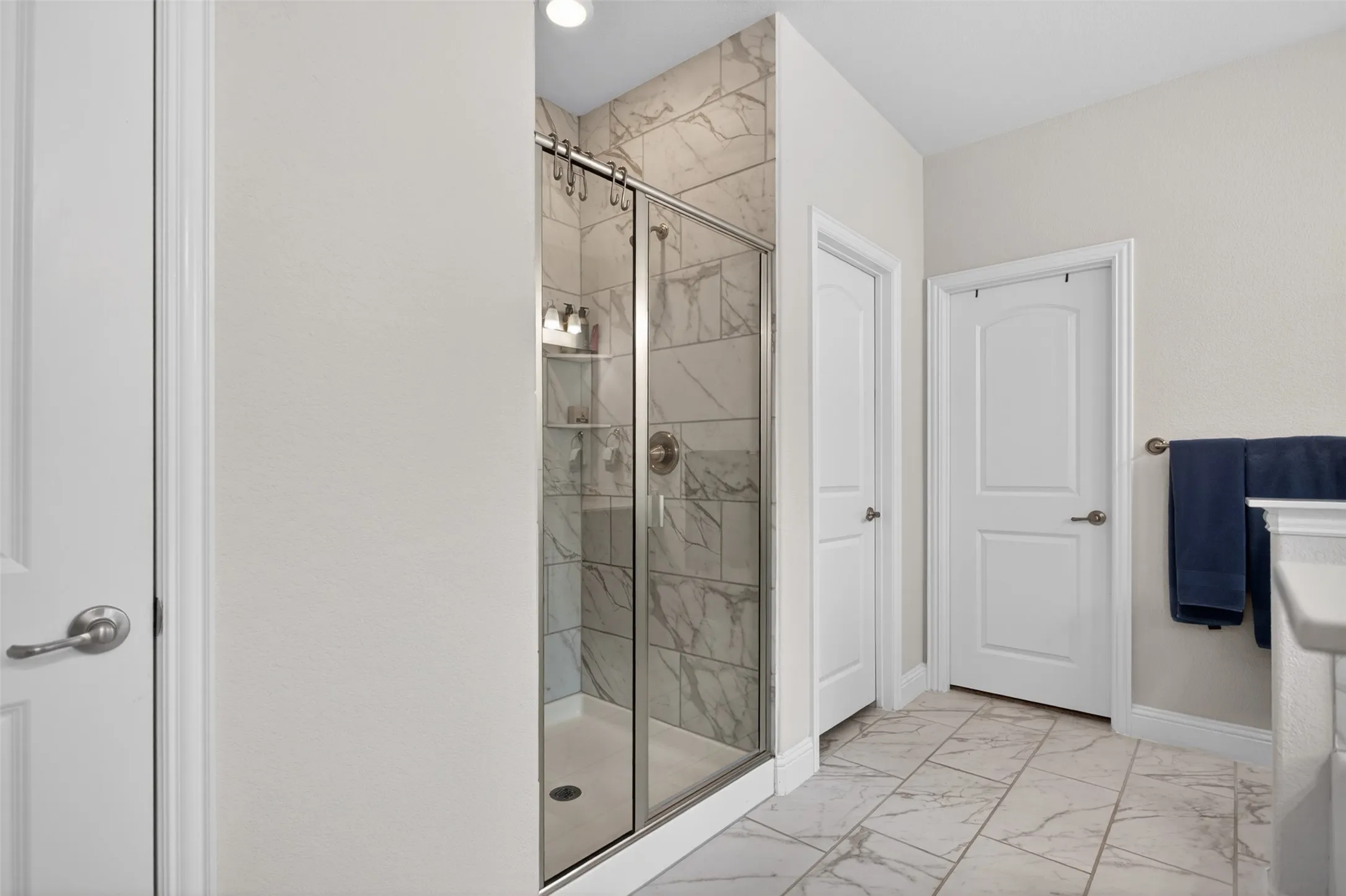 Shower enclosure with clear glass door and brushed nickel hardware, featuring white and gray veined tile surround