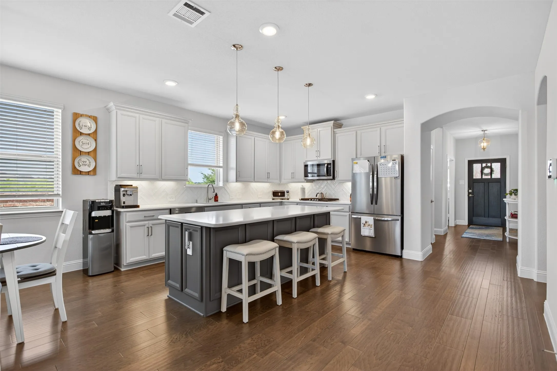 Kitchen featuring wood-finish flooring, an island with countertop seating, white cabinetry, a tile backsplash, and stainless steel appliances