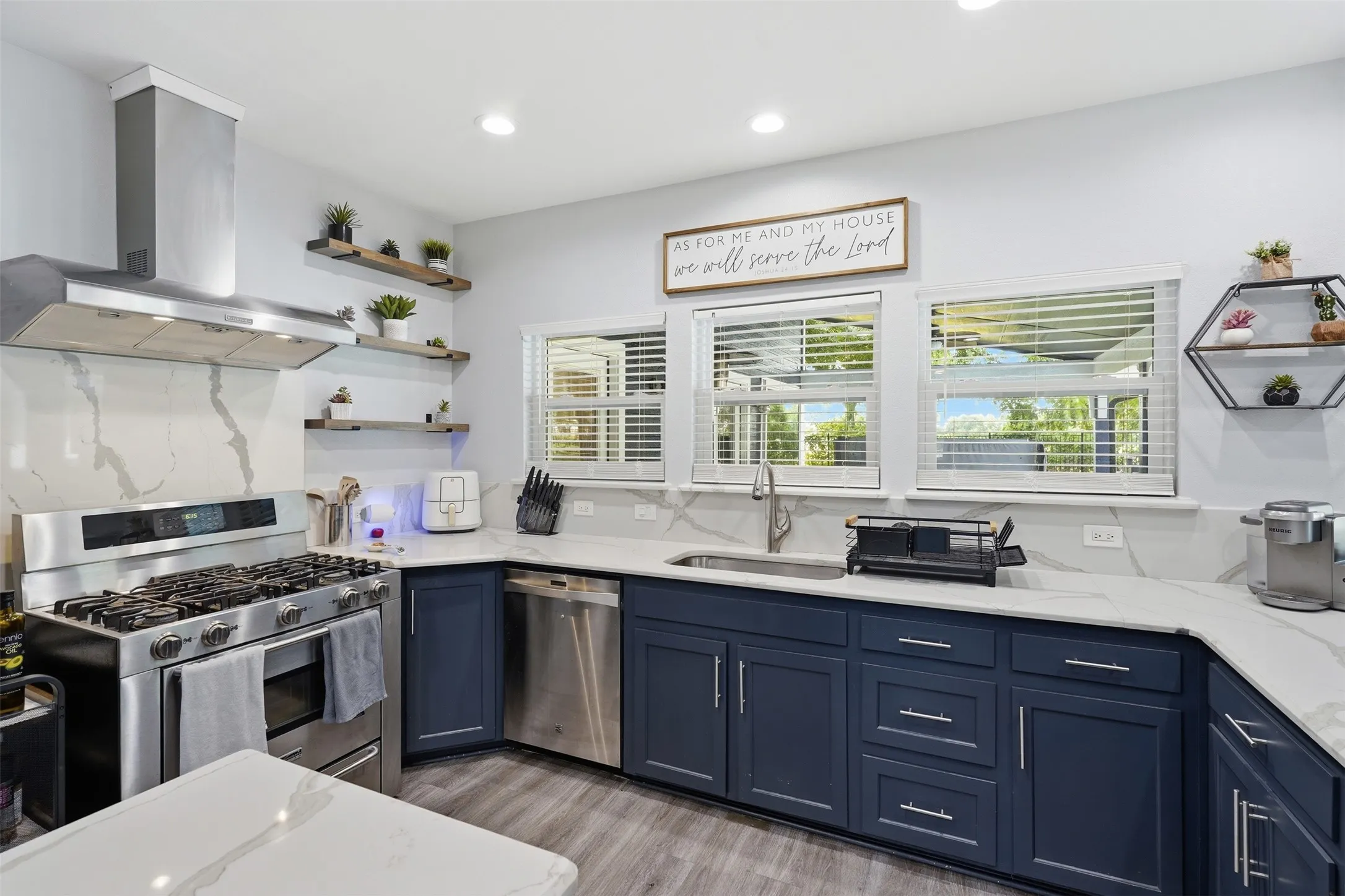 Modern kitchen featuring dark blue cabinetry, light countertops with prominent veining, and a stainless steel appliance suite