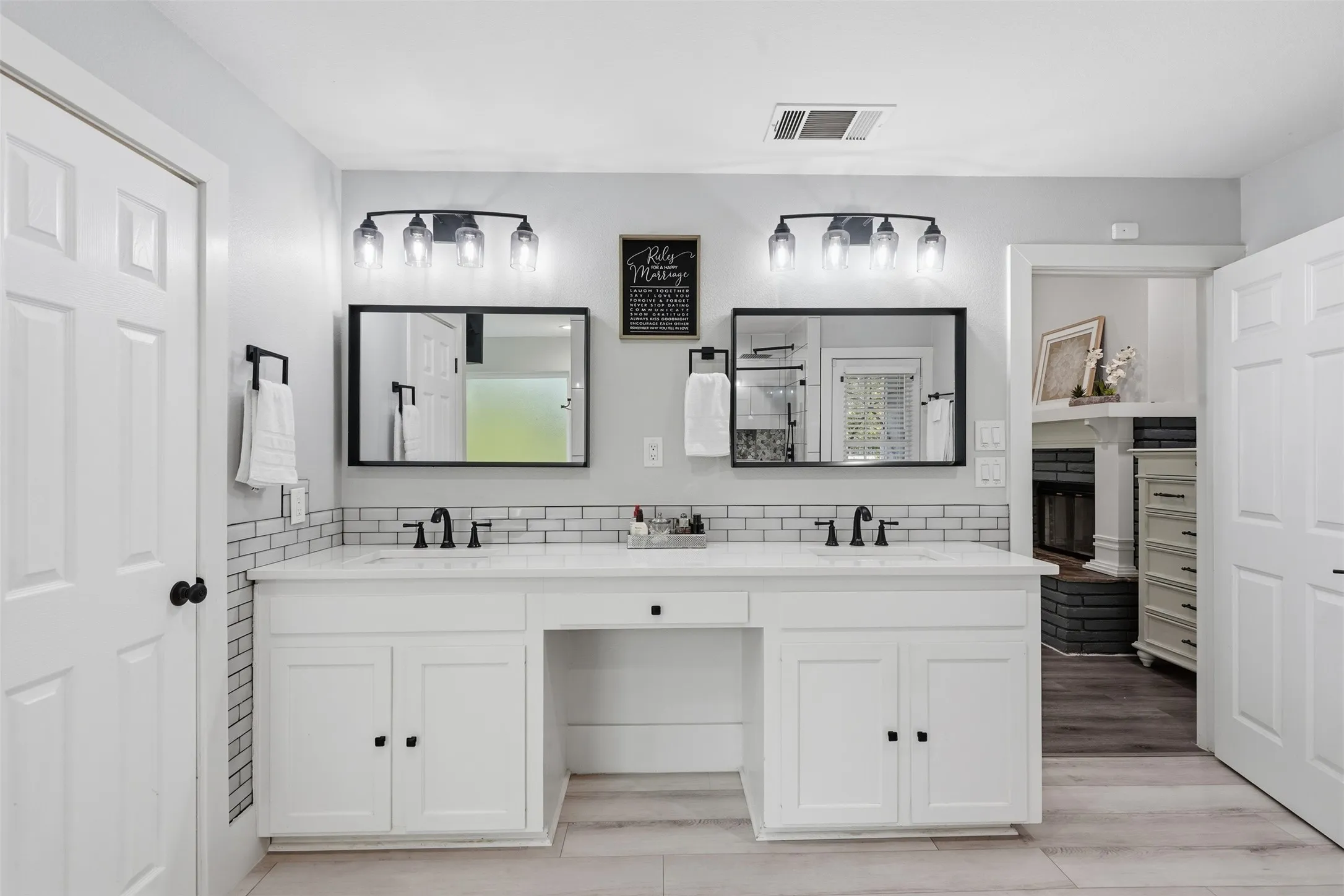 Dual vanity with white cabinetry and integrated sinks, matte black fixtures, subway tile backsplash, and wood-finish flooring