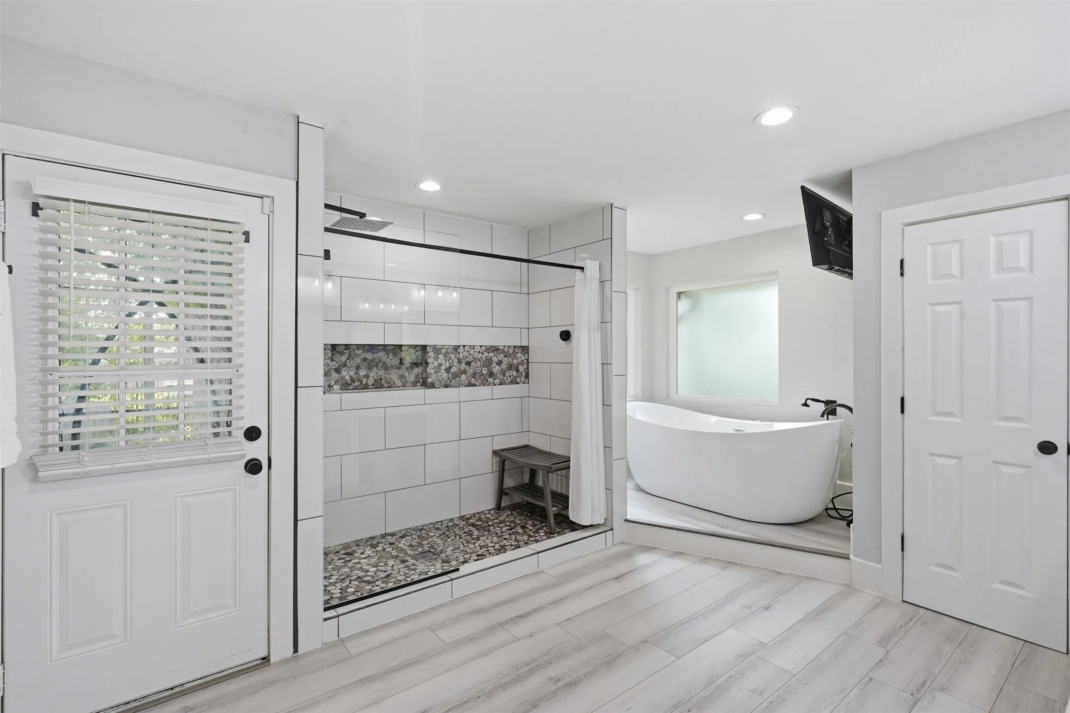 Modern bathroom featuring a freestanding soaking tub, a walk-in shower with mosaic pebble flooring and accent tile, and light wood-finish flooring