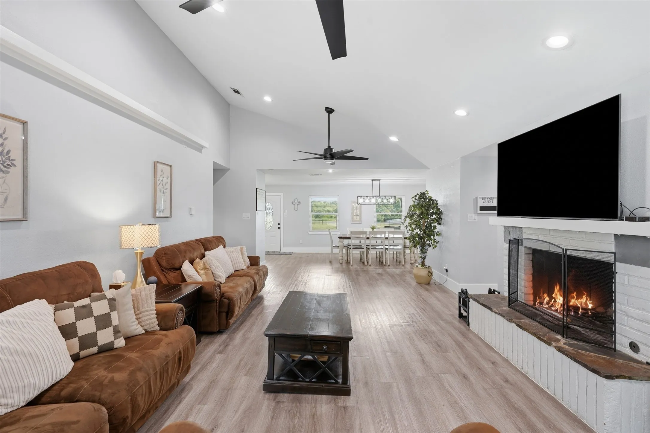 Spacious living area featuring high vaulted ceilings, recessed lighting, wood-finish flooring, and a brick fireplace with a stone hearth