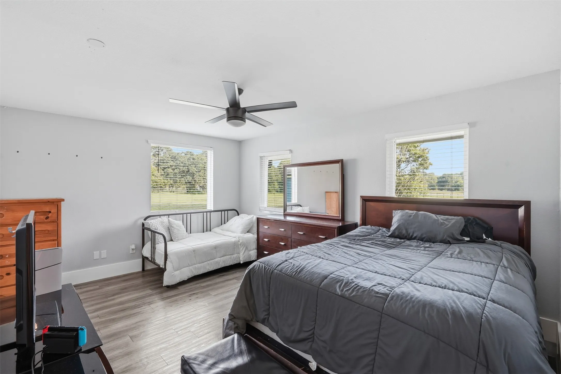 Spacious bedroom featuring light gray walls, wood-finish flooring, and multiple windows