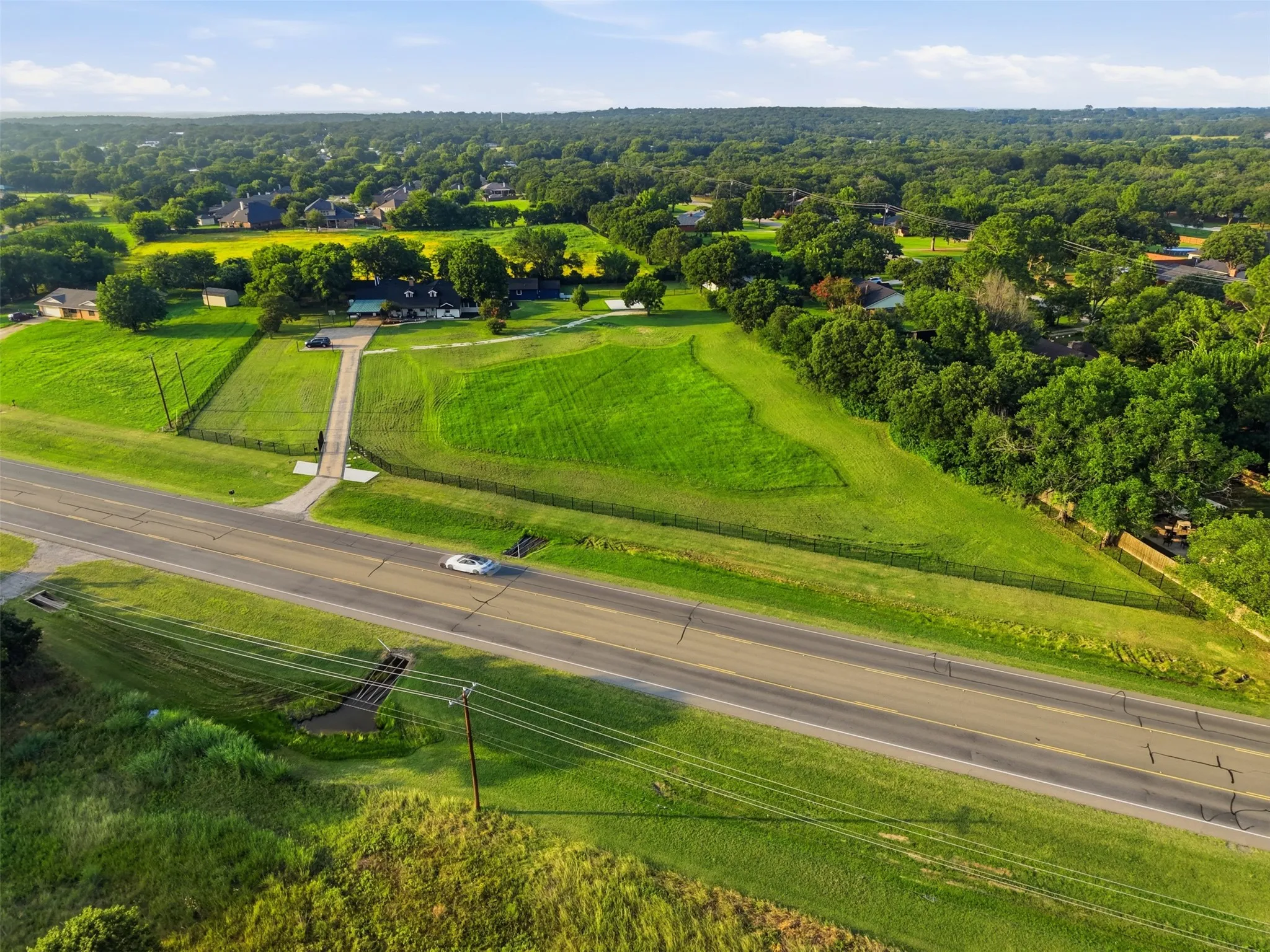 Expansive property featuring a paved driveway, established landscaping, mature trees, and a perimeter fence