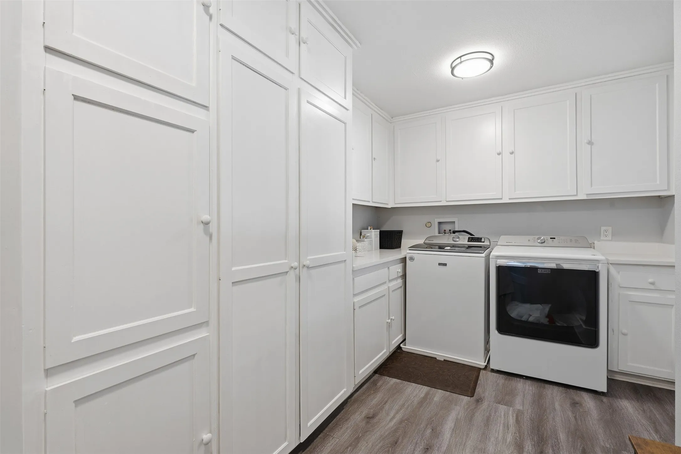 Laundry room featuring extensive white built-in cabinetry, upper and lower storage, white countertops, and wood-finish flooring