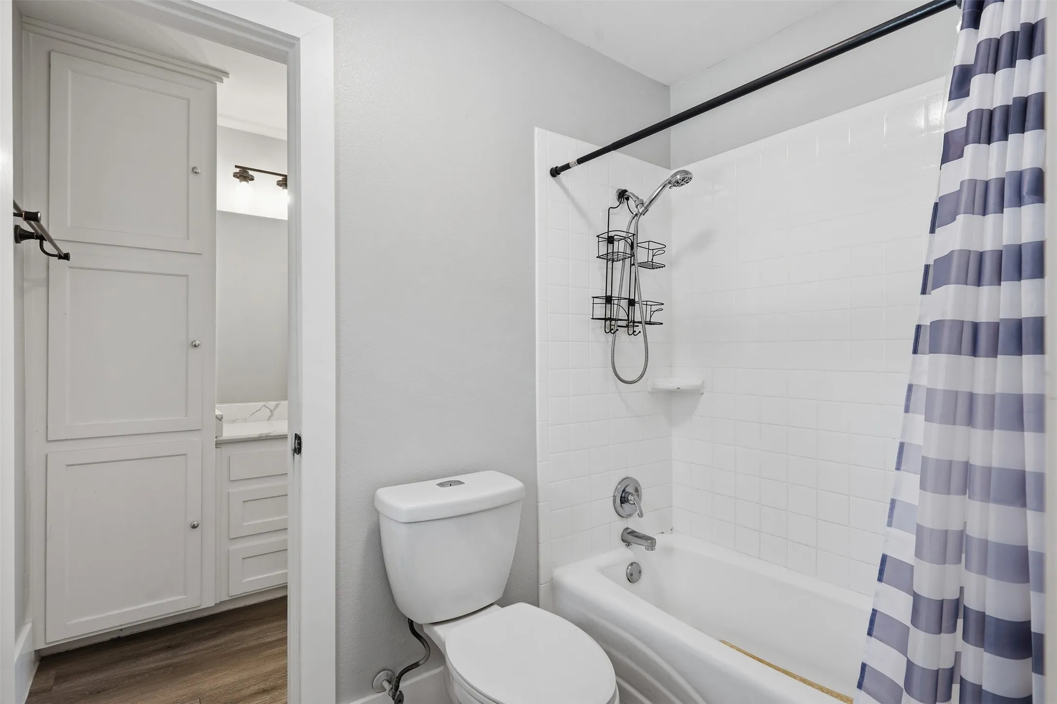 Bathroom featuring a full tub and shower combination with white subway tile surround, white toilet, and wood-finish flooring