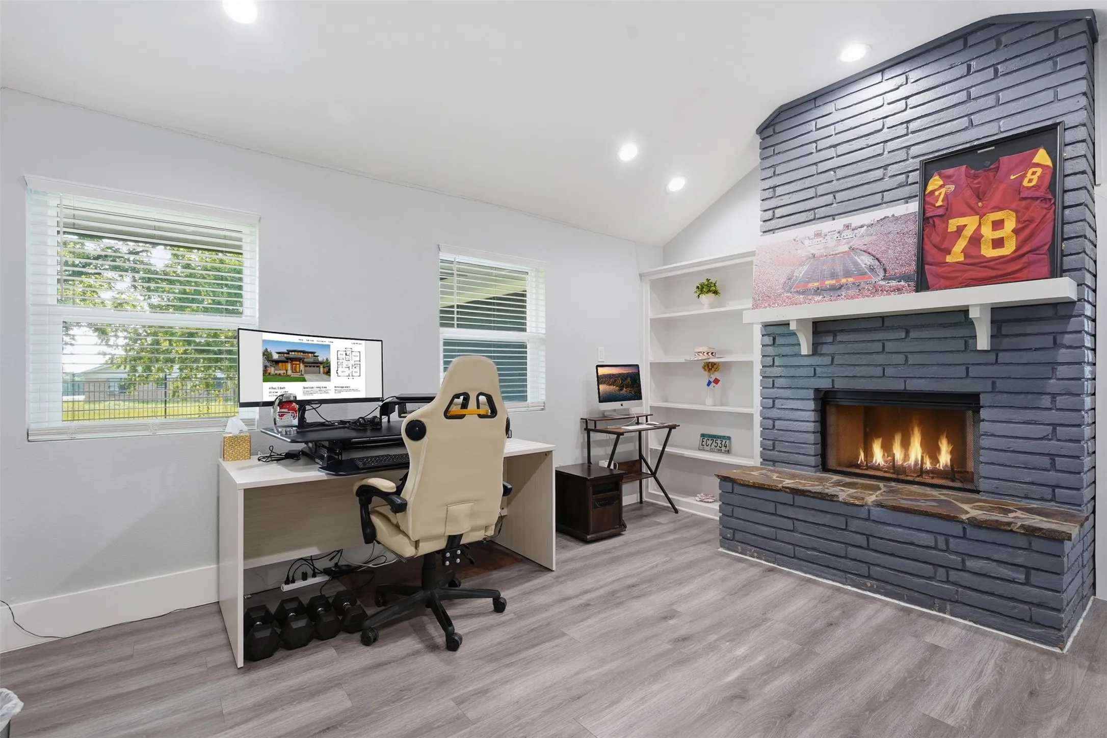 Vaulted ceiling interior featuring recessed lighting, gray wood-finish flooring, and a painted brick fireplace with a stone hearth