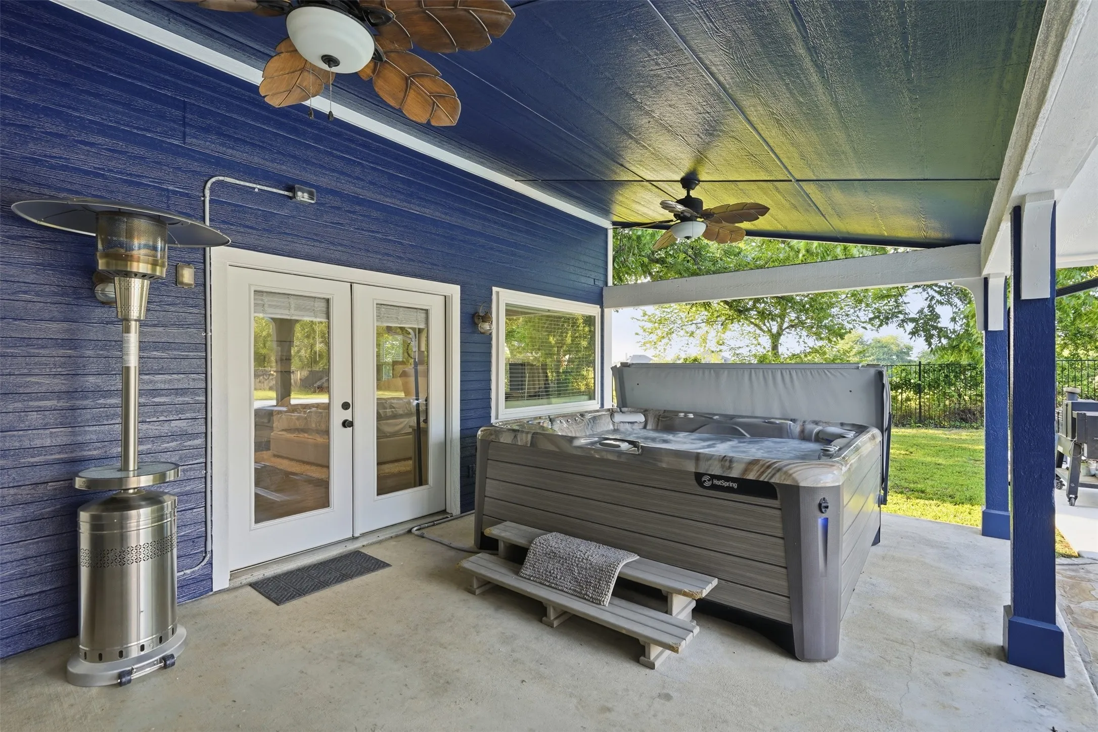 Covered patio featuring a hot tub, concrete flooring, dual ceiling fans, and a vibrant blue exterior wall