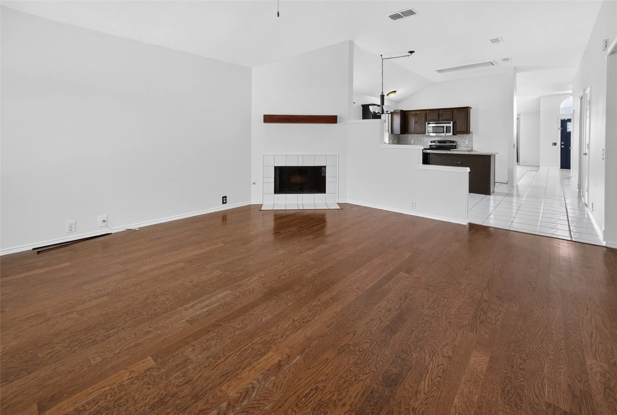 Open-concept living space featuring wood-finish flooring, a fireplace with a white tile surround, and an exposed wood mantel