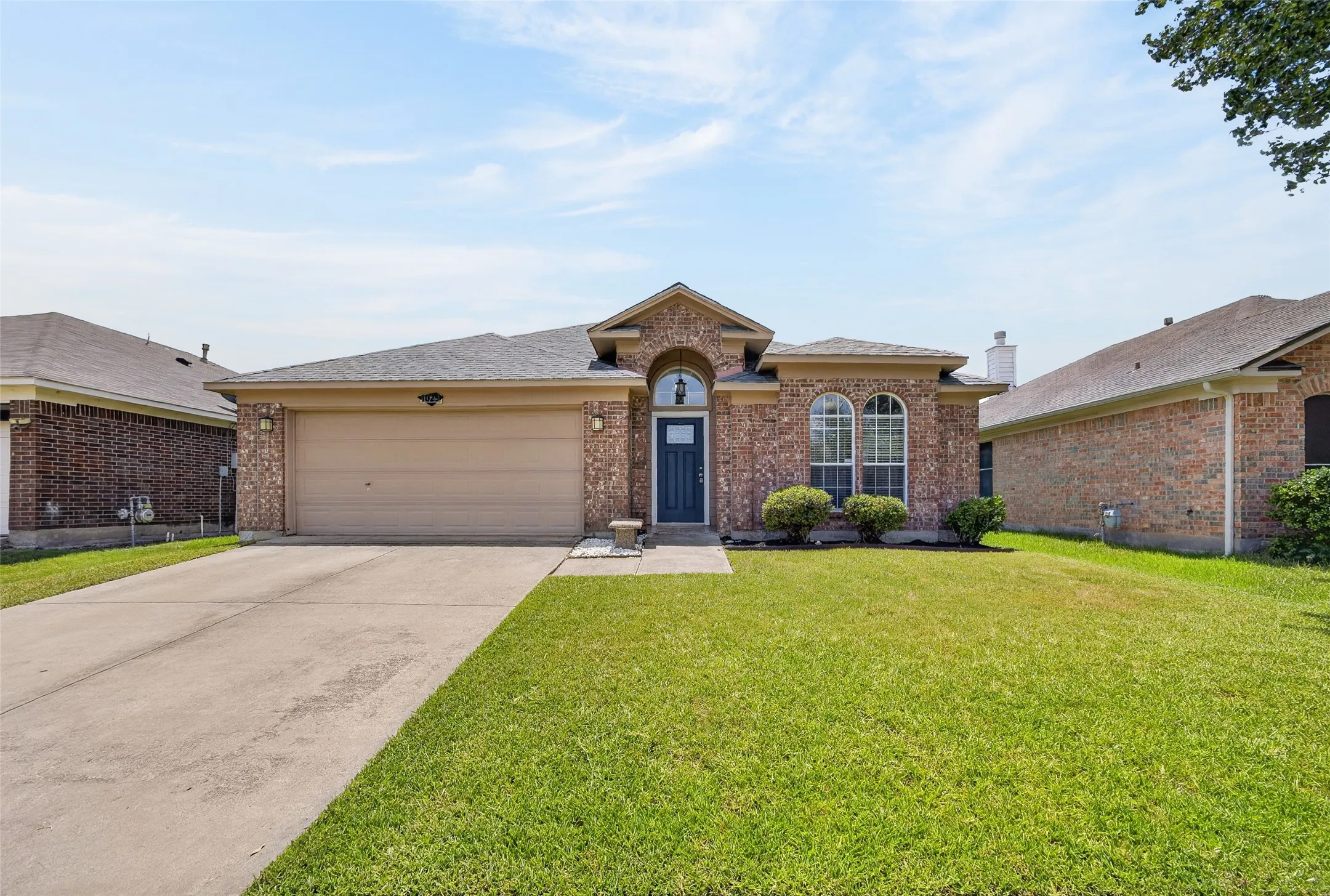 Brick facade residence featuring an attached two-car garage, arched front windows, a dark blue front door, and a concrete driveway