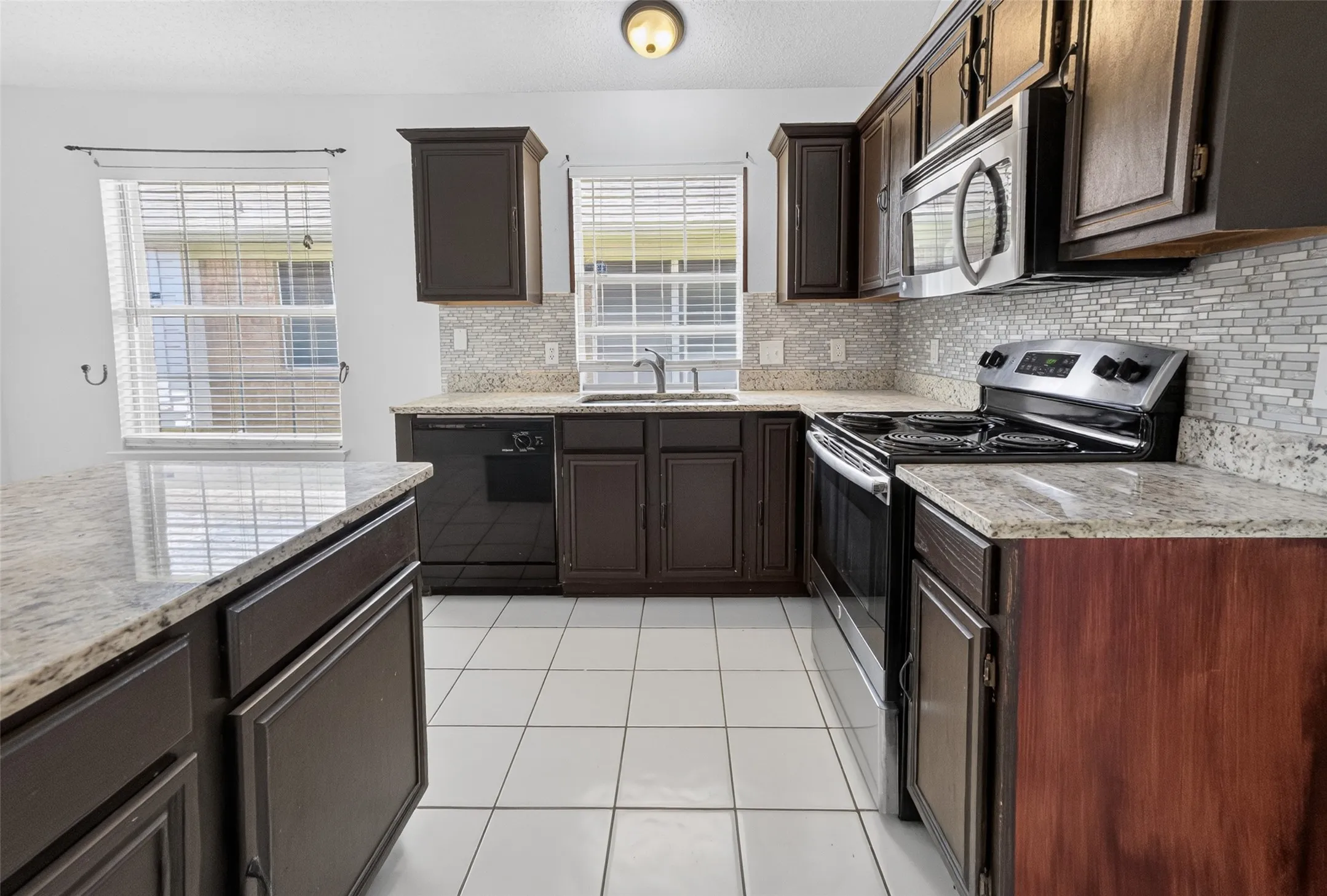 Kitchen featuring dark wood cabinetry, light-toned granite countertops, and a full tile backsplash