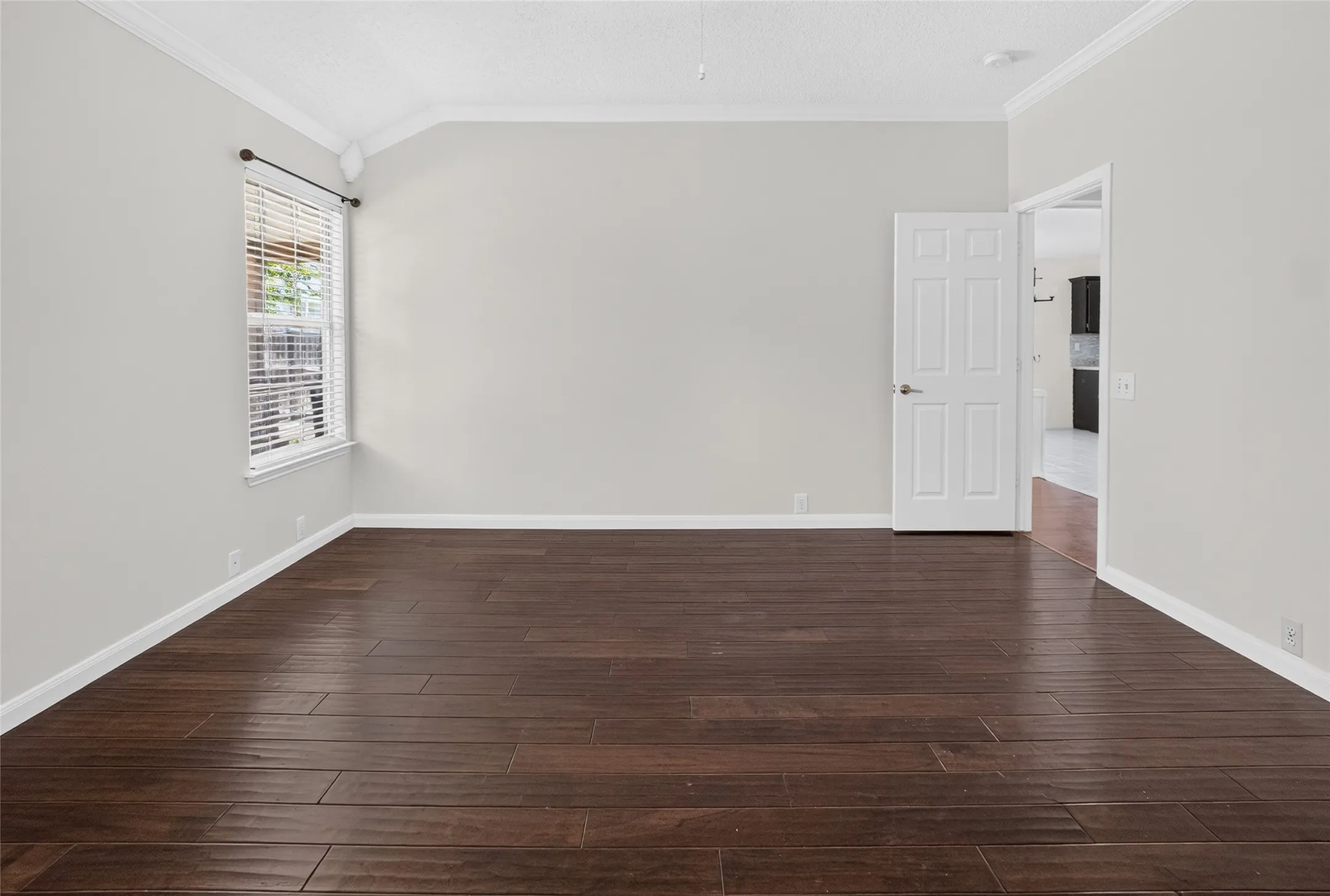 Spacious room featuring wood-finish flooring, light gray walls, white baseboards, and crown molding