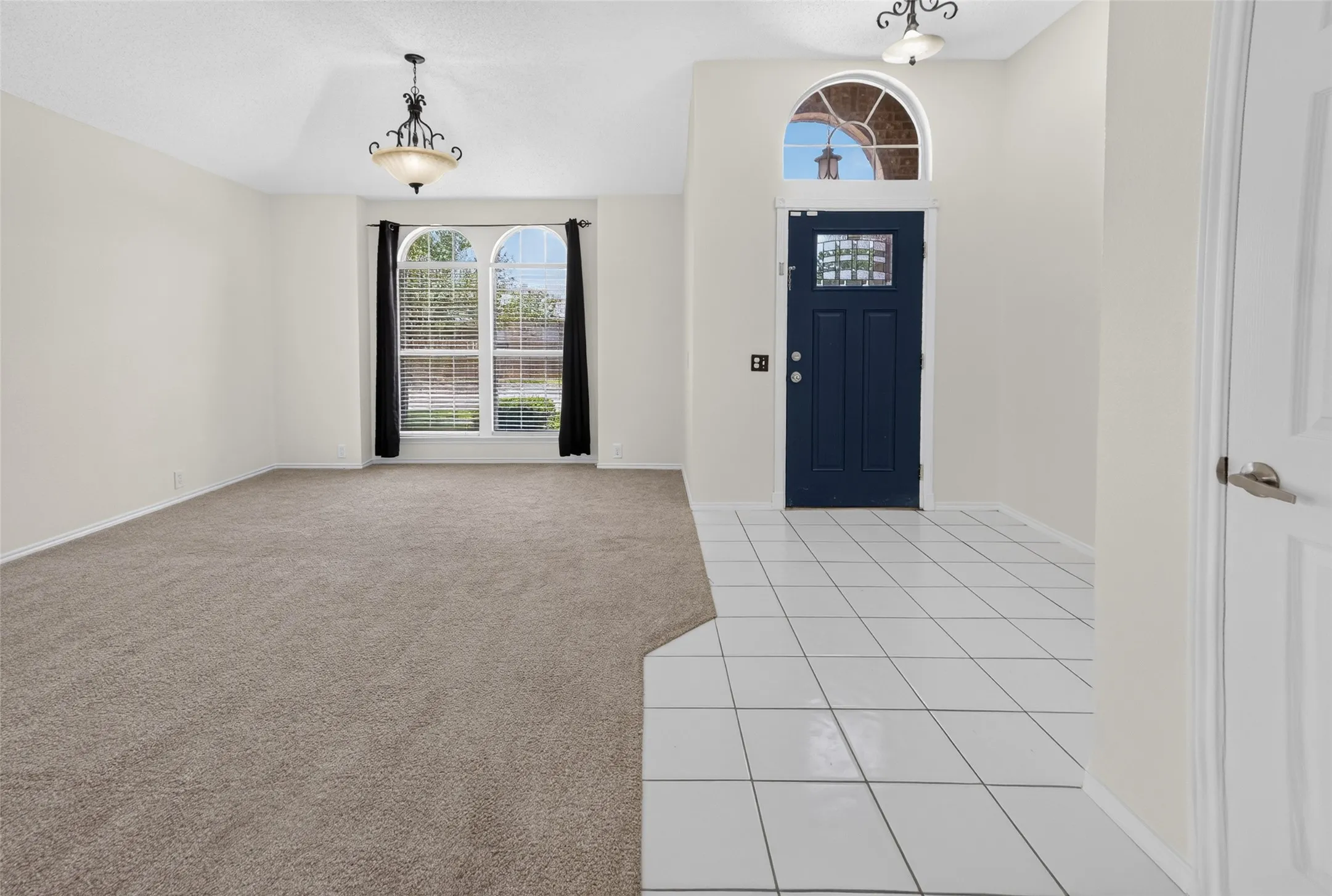 Entryway featuring a dark blue front door with decorative glass, an arched transom window, and white square tile flooring
