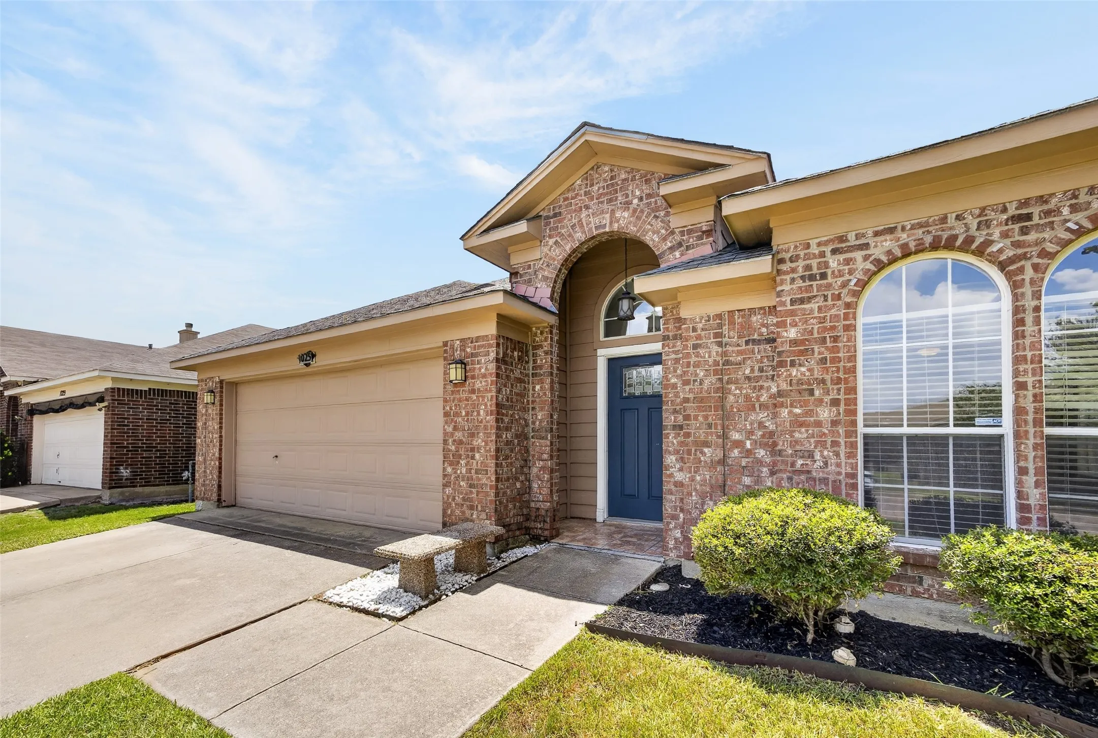 Brick exterior featuring an arched entryway, a deep blue front door, an attached two-car garage, and arched windows