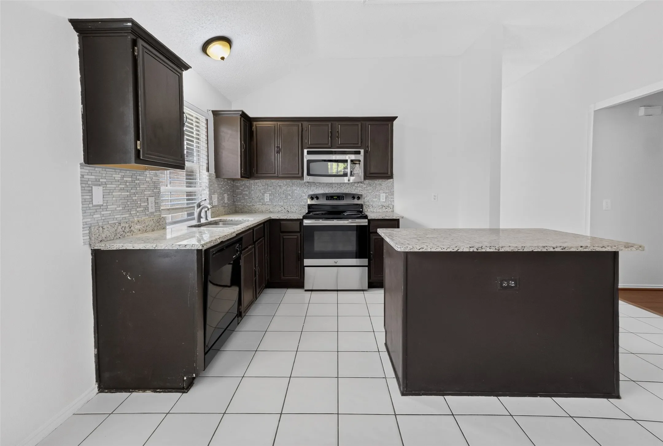 Kitchen featuring a central island with a light-colored countertop, dark wood-finish cabinetry, a tile backsplash, and stainless steel appliances