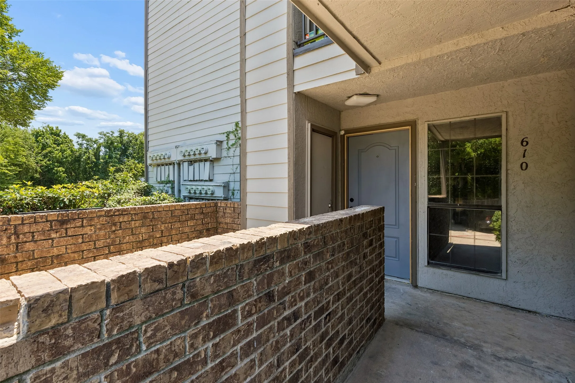 Brick privacy wall framing an entryway with a light-toned door, an adjacent window, and concrete flooring