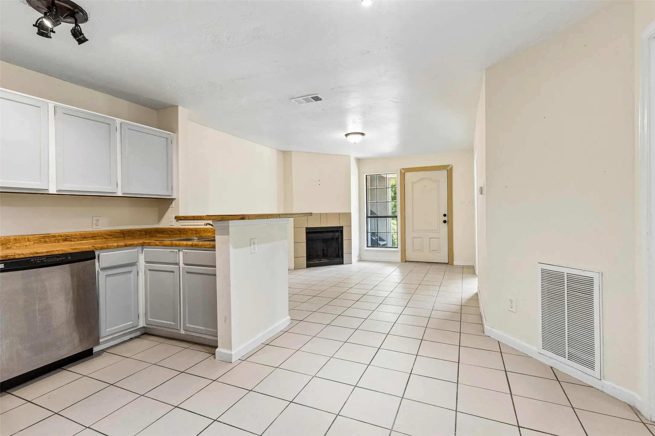 Open-concept living space with tile flooring, a fireplace, and a kitchen featuring white cabinetry, a breakfast bar, and a stainless steel dishwasher