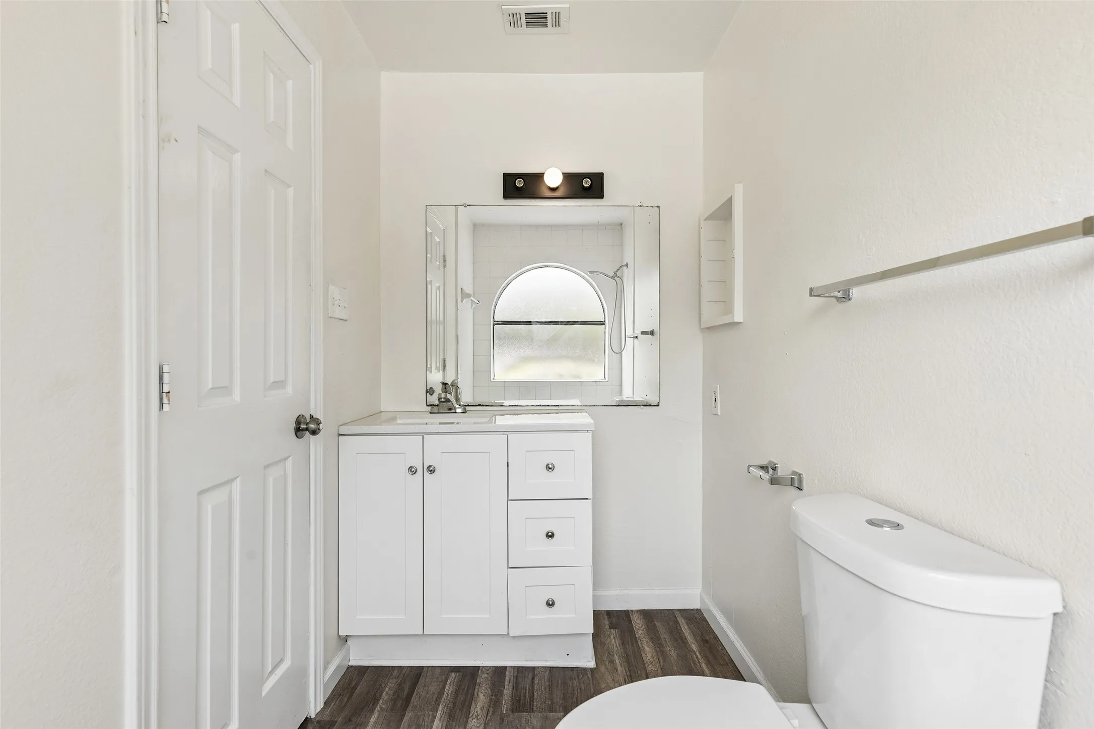 Bathroom featuring a white vanity with integrated sink, chrome faucet, wall-mounted mirror, and wood-finish flooring