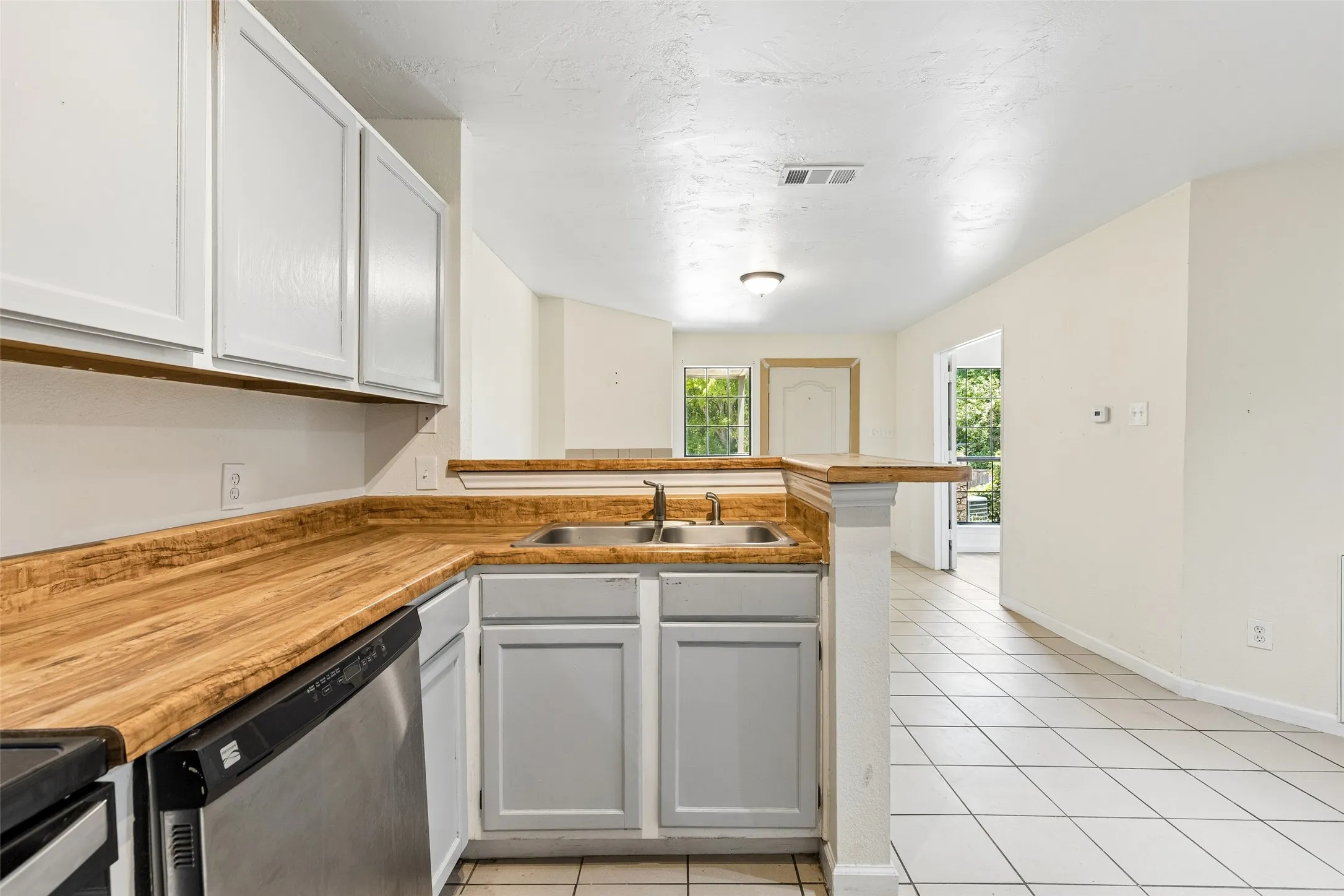 Kitchen featuring wood-finish countertops, stainless steel double basin sink, white upper cabinetry, and gray lower cabinetry