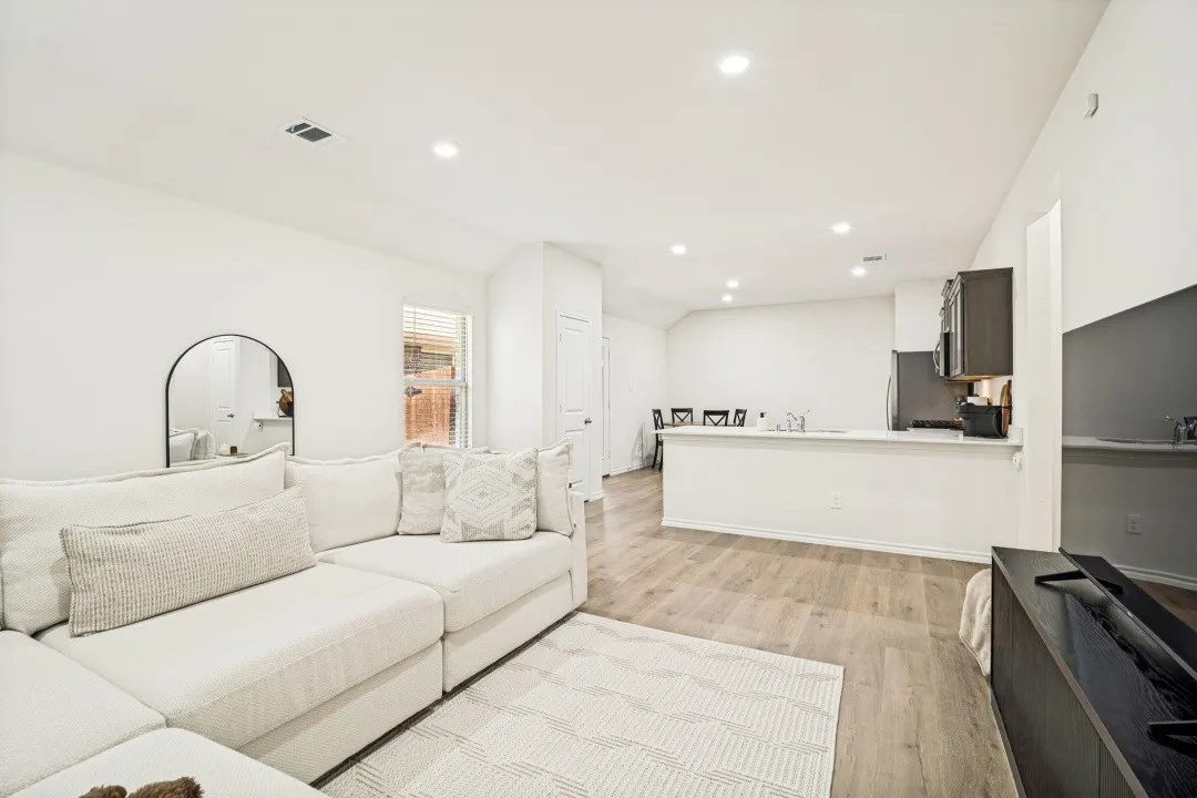 Open-concept living area with wood-finish flooring, recessed lighting, and a kitchen featuring dark cabinetry and a light-toned countertop