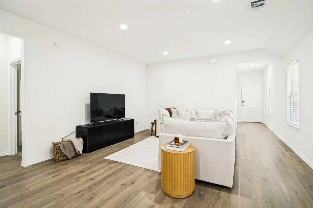 Spacious living area featuring wood-finish flooring, recessed lighting, white walls, and multiple windows with blinds