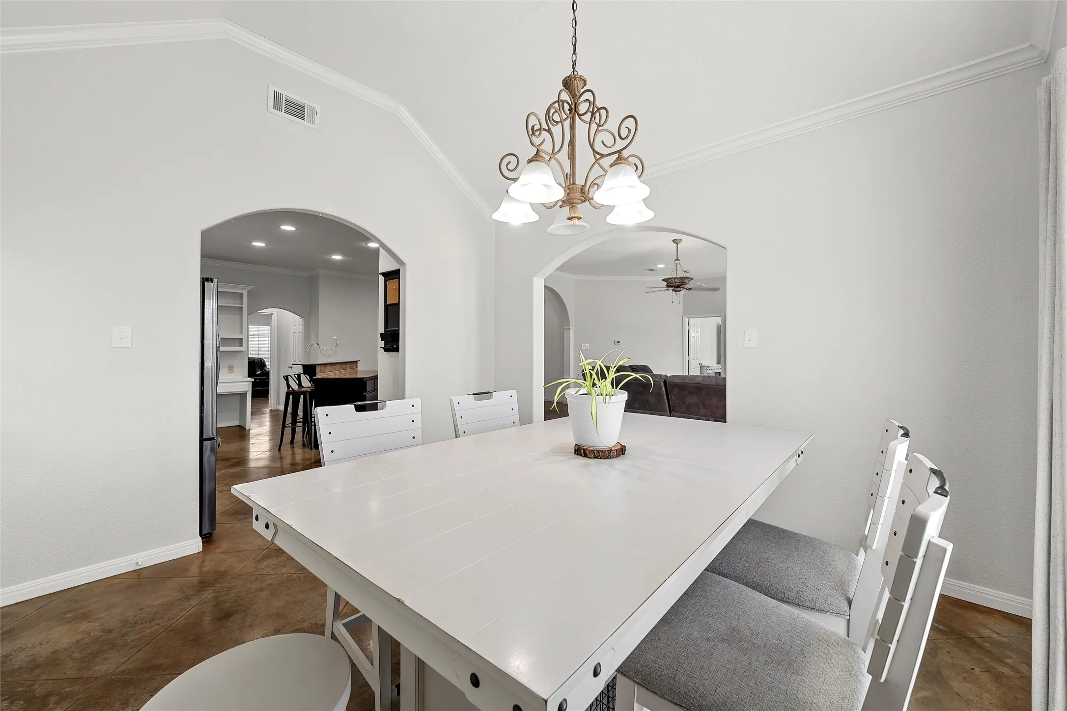 Dining area featuring a decorative chandelier, crown molding, arched doorways, and concrete flooring