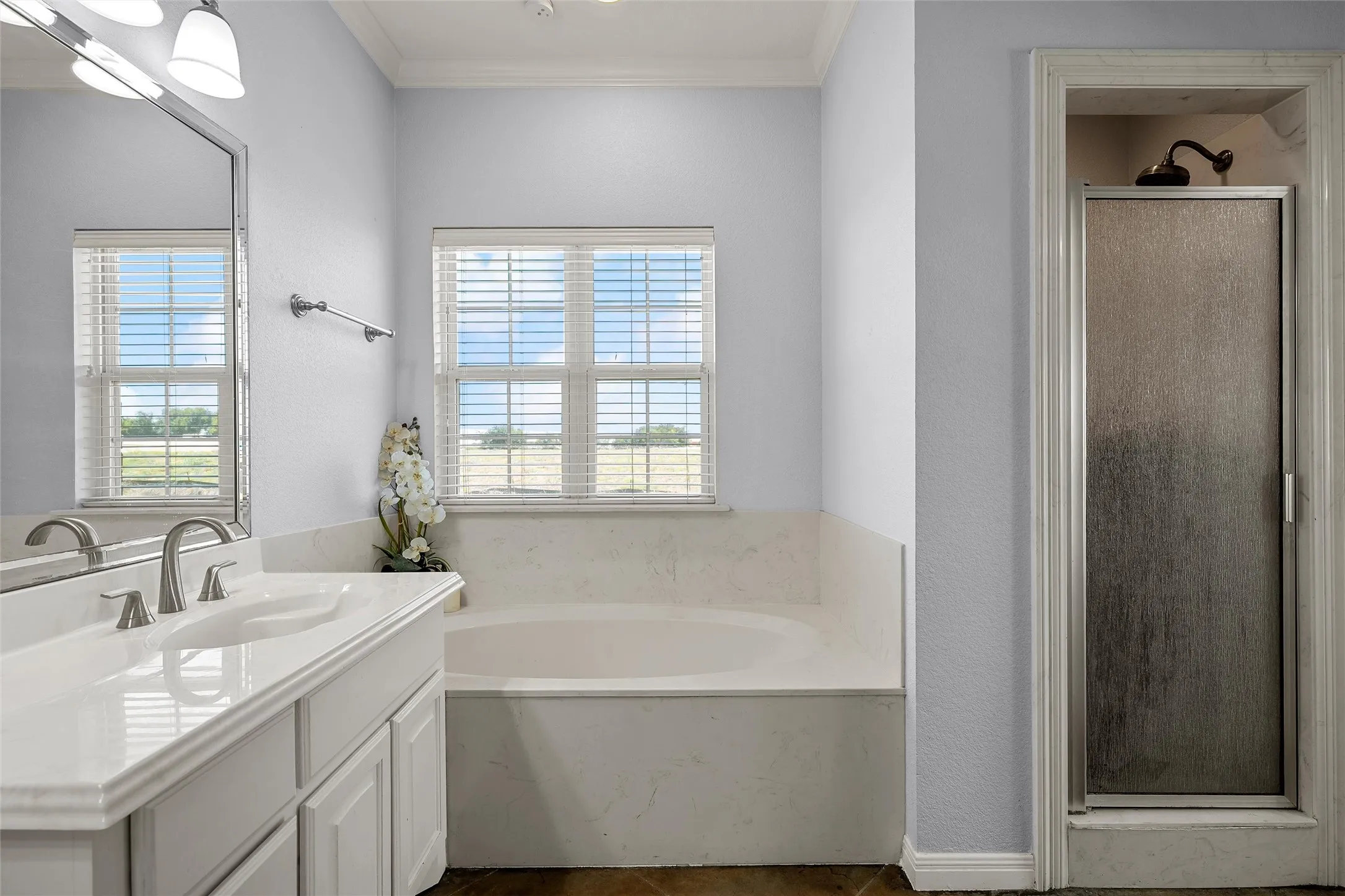 Bathroom featuring a built-in soaking tub, a separate shower enclosure with a frosted glass door, a vanity with an integrated sink, and a framed mirror