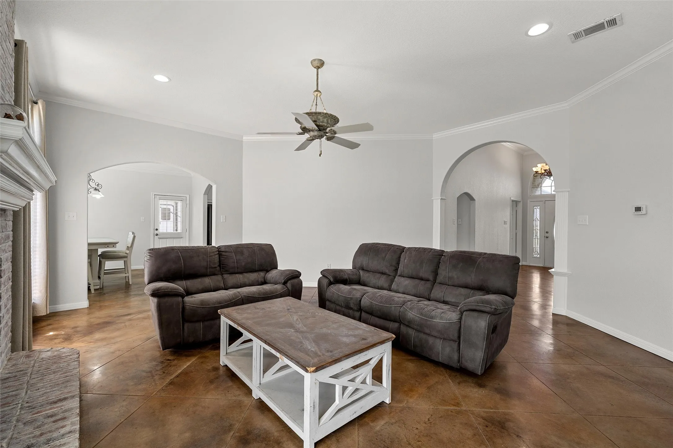 Spacious living area featuring polished concrete flooring, arched doorways, a brick fireplace with a white mantel, recessed lighting, and crown molding