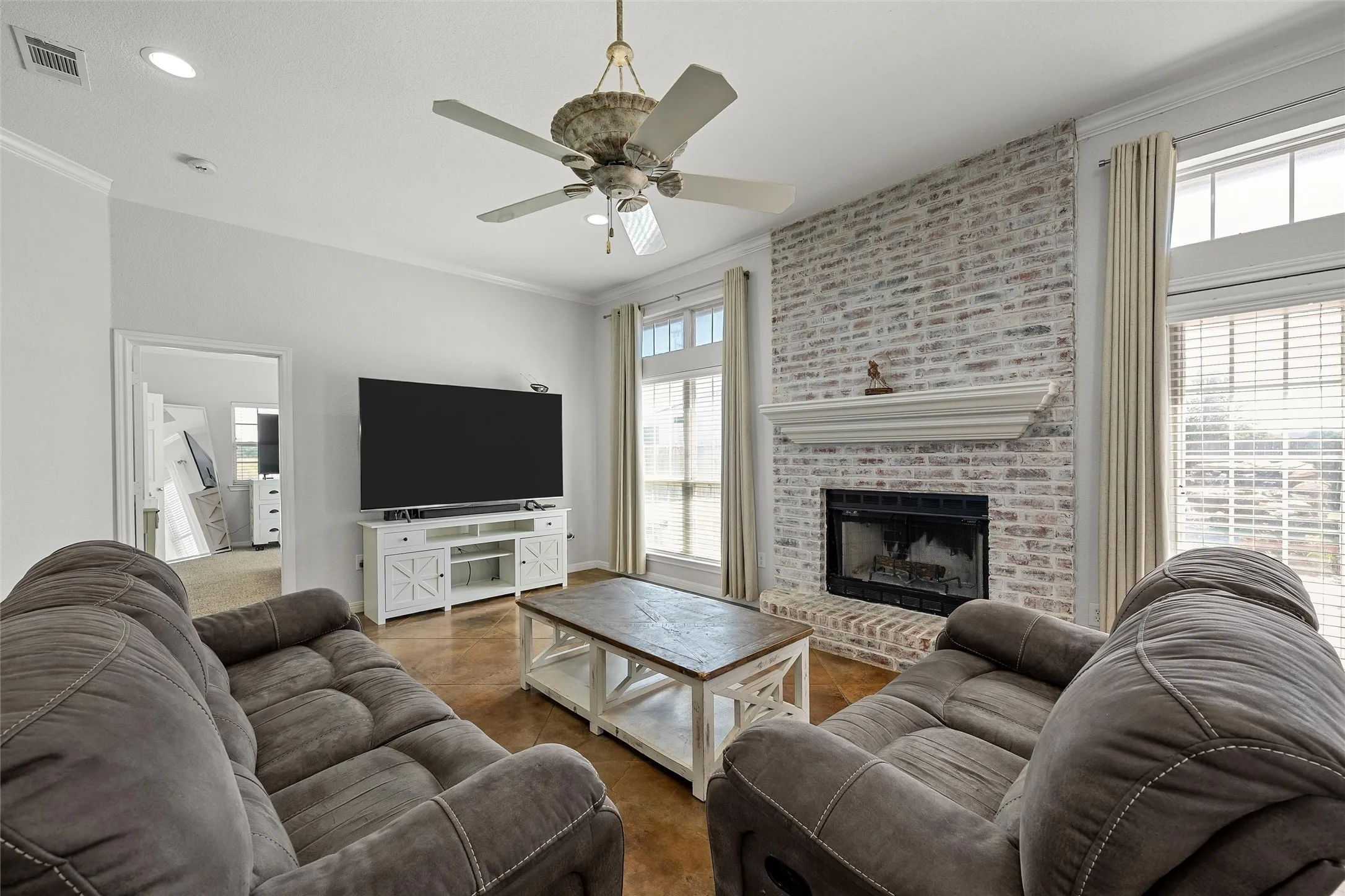 Living room featuring a prominent brick fireplace with a white mantel, high ceilings with a ceiling fan, and recessed lighting