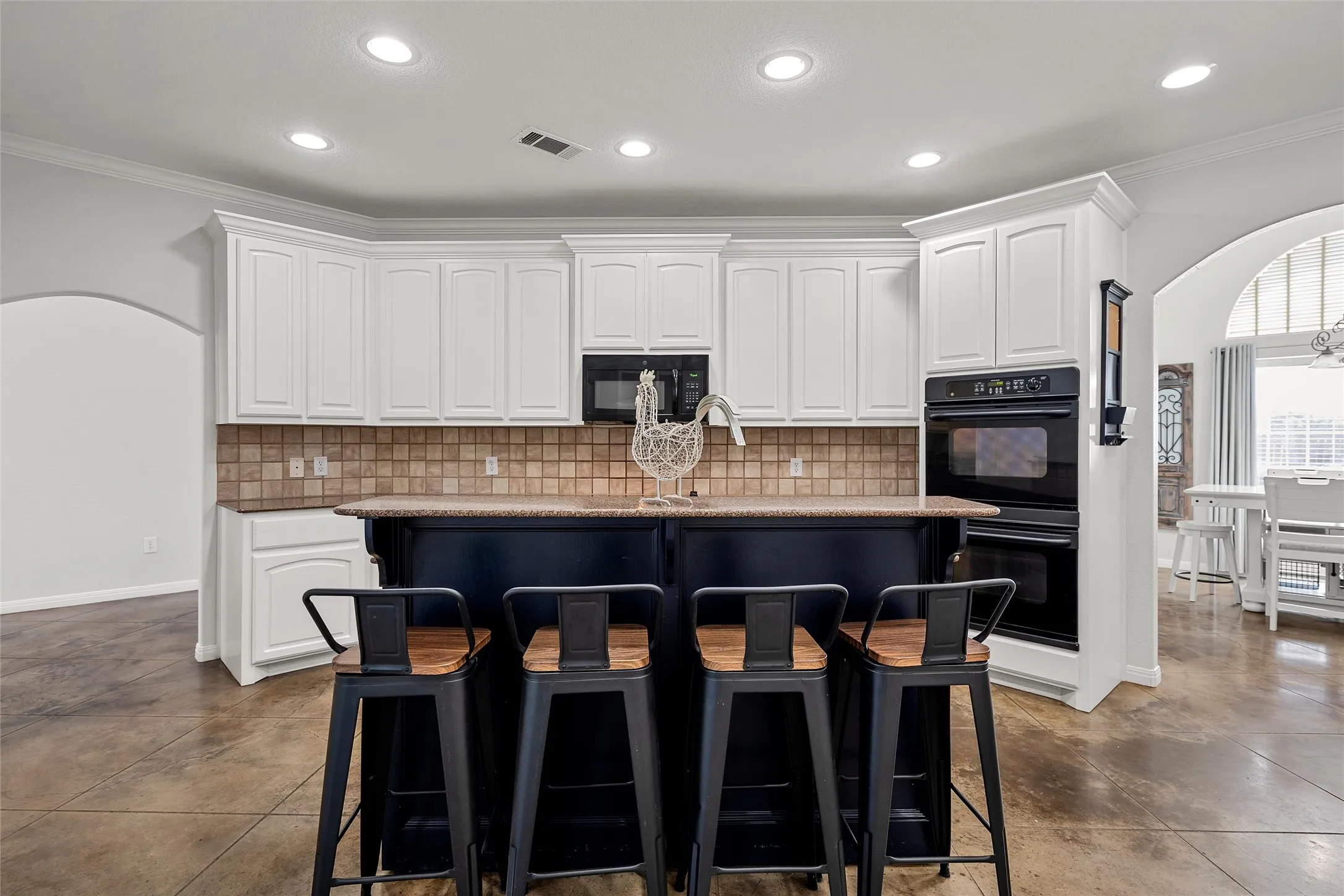 Spacious kitchen featuring an expansive central island, white cabinetry, integrated black double ovens, a built-in microwave, and tile backsplash