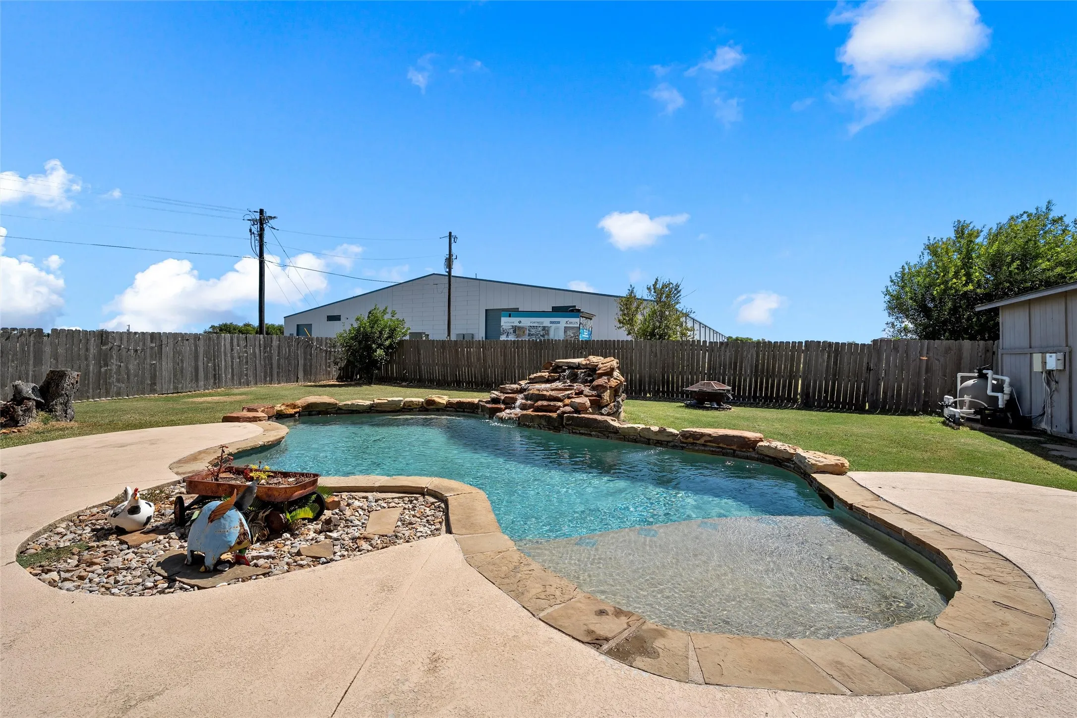 Freeform swimming pool featuring a rock waterfall, flagstone coping, and a surrounding concrete patio